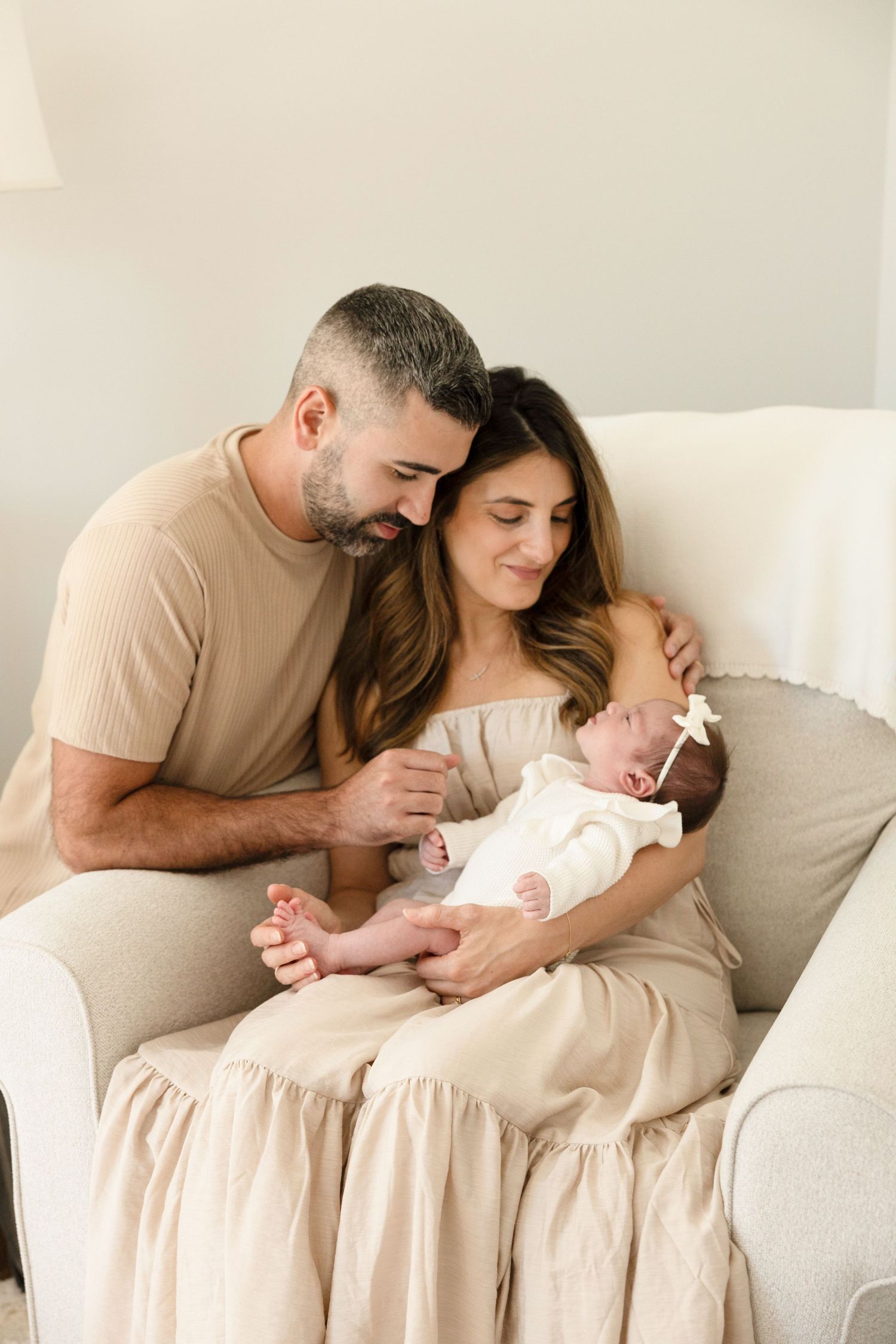 Family cuddles together on white couch during intimate newborn photo session.