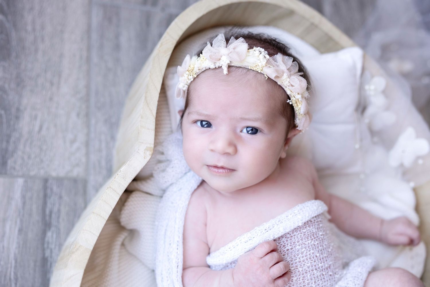 Baby wearing white bonnet lies on soft blanket during portrait session.