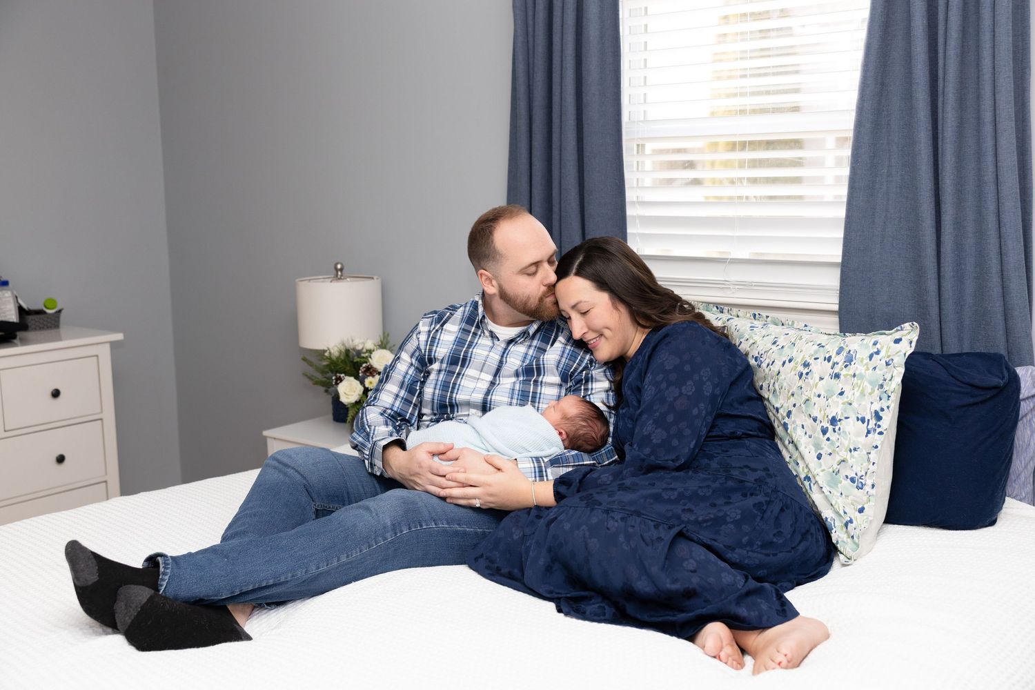Family sharing tender moment with newborn on bed in modern bedroom.