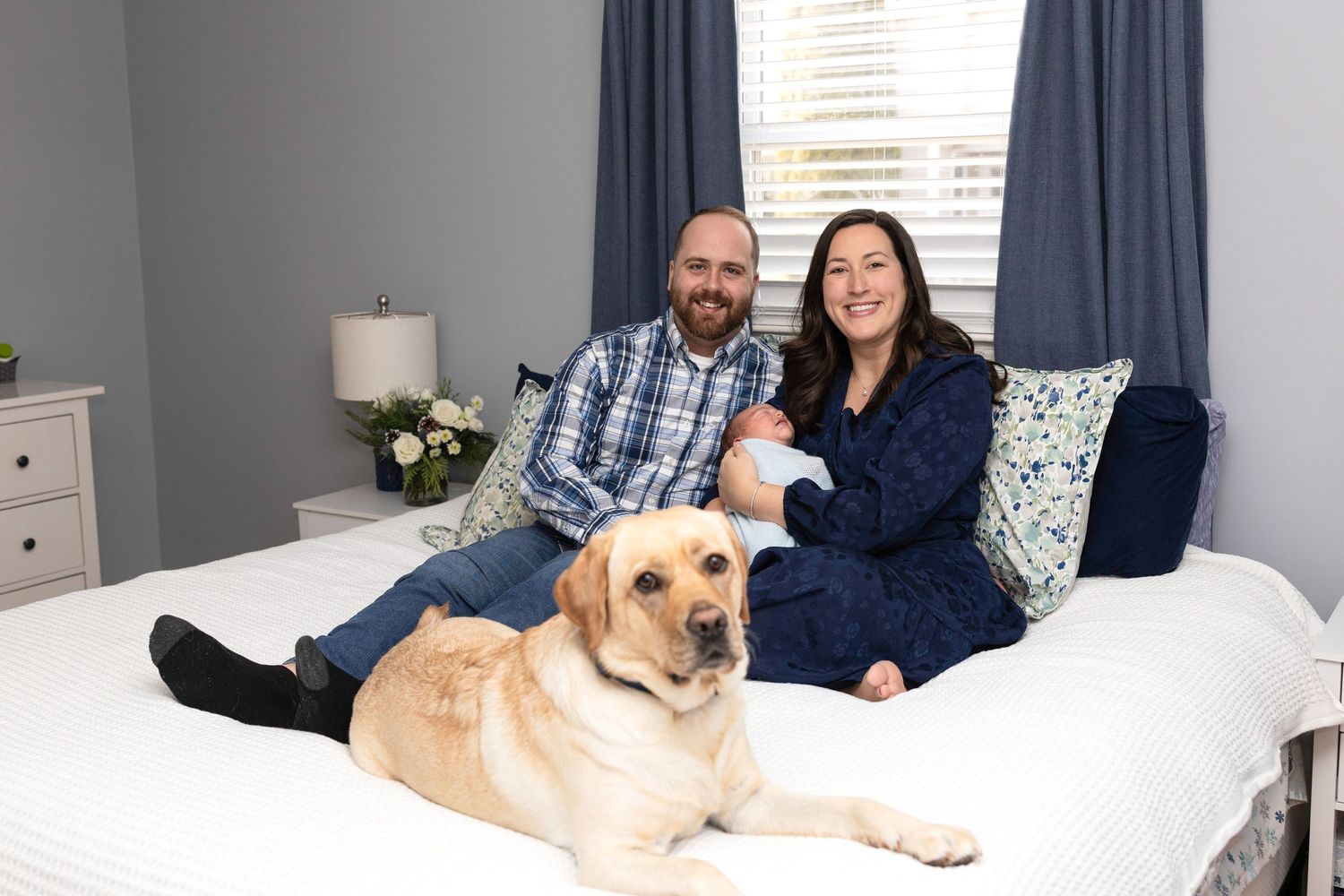 Family relaxing on bed with golden retriever in blue and white bedroom.