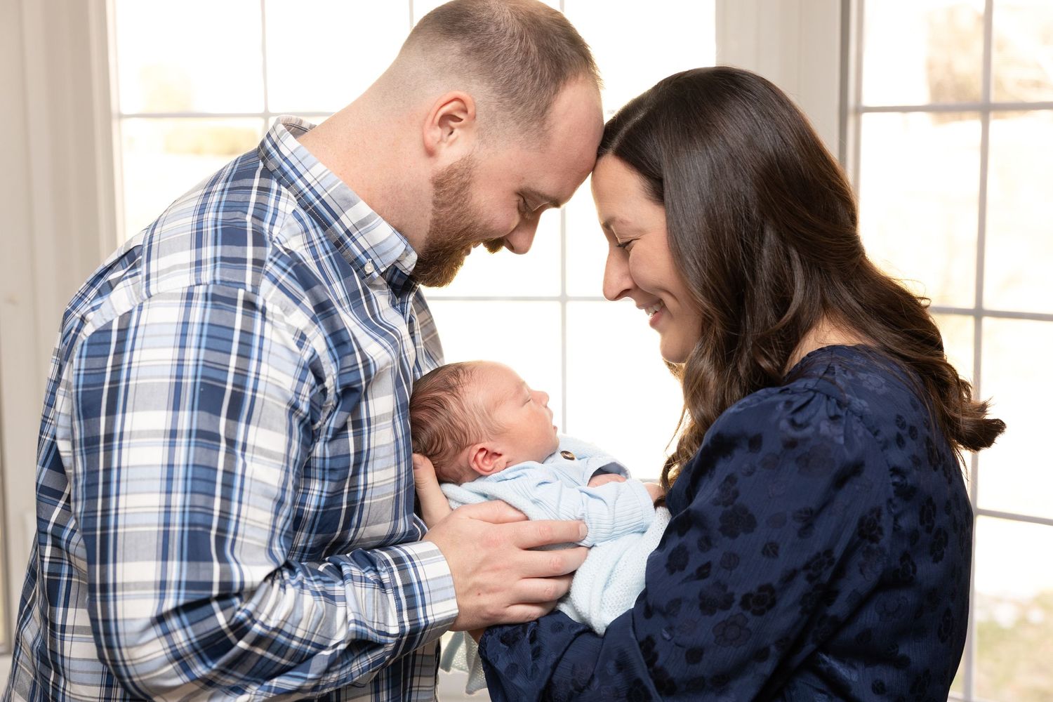 Intimate family moment with newborn in natural window light.