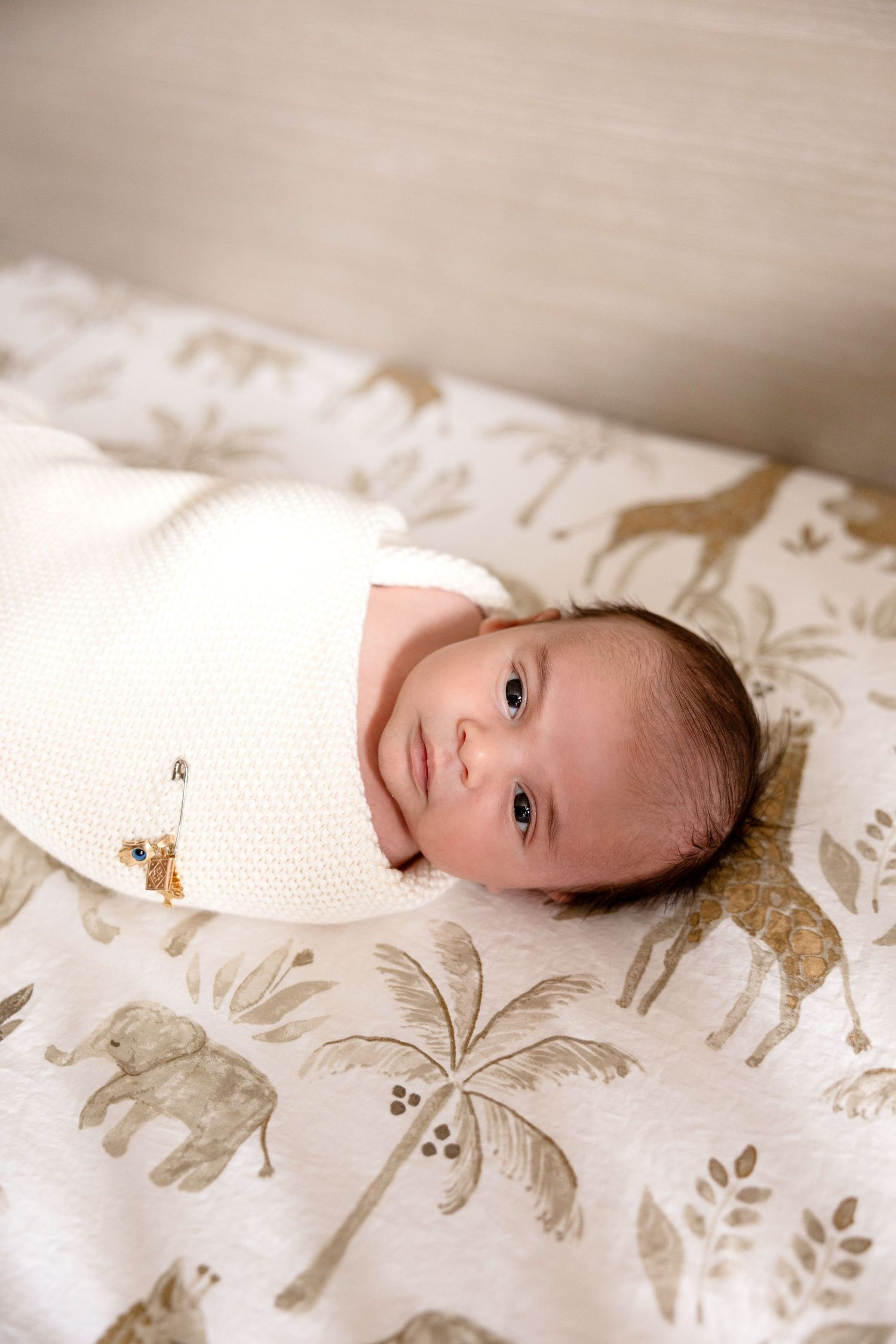 Newborn baby swaddled in white wrap lying on safari animal print blanket with elephants and giraffes.