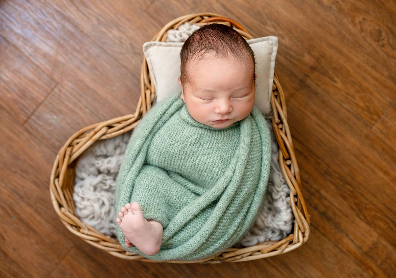 Sleeping newborn in mint green wrap nestled in wicker basket.
