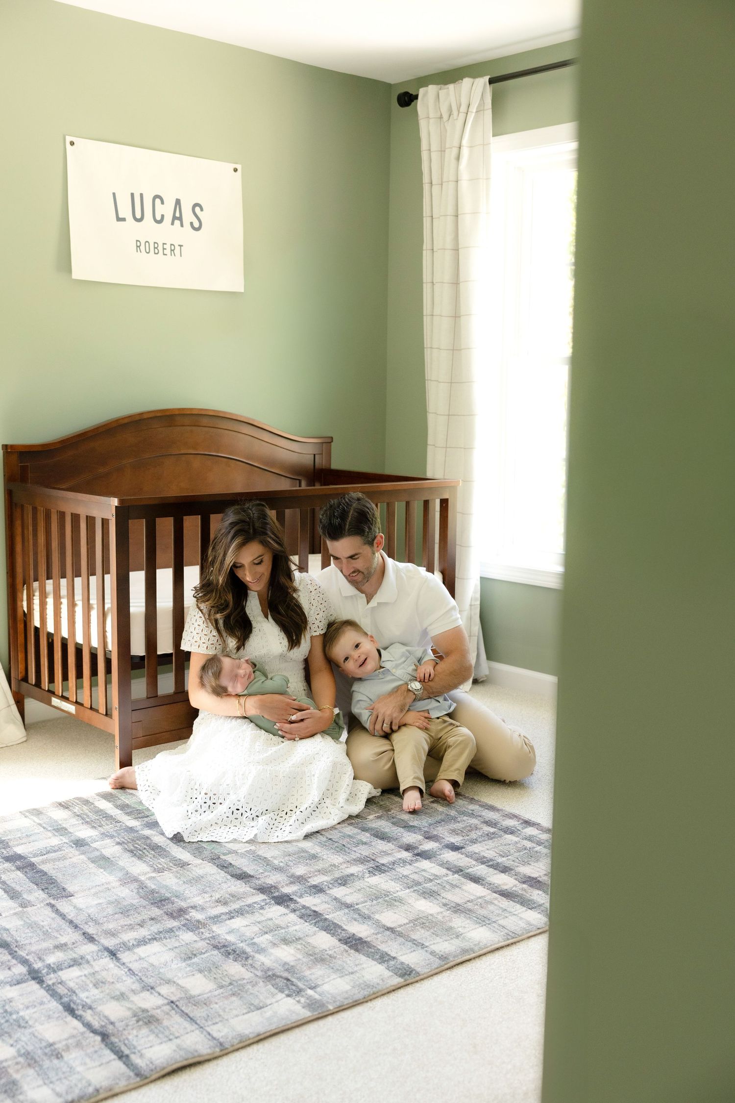 Family relaxing together on plaid blanket in nursery with green walls.