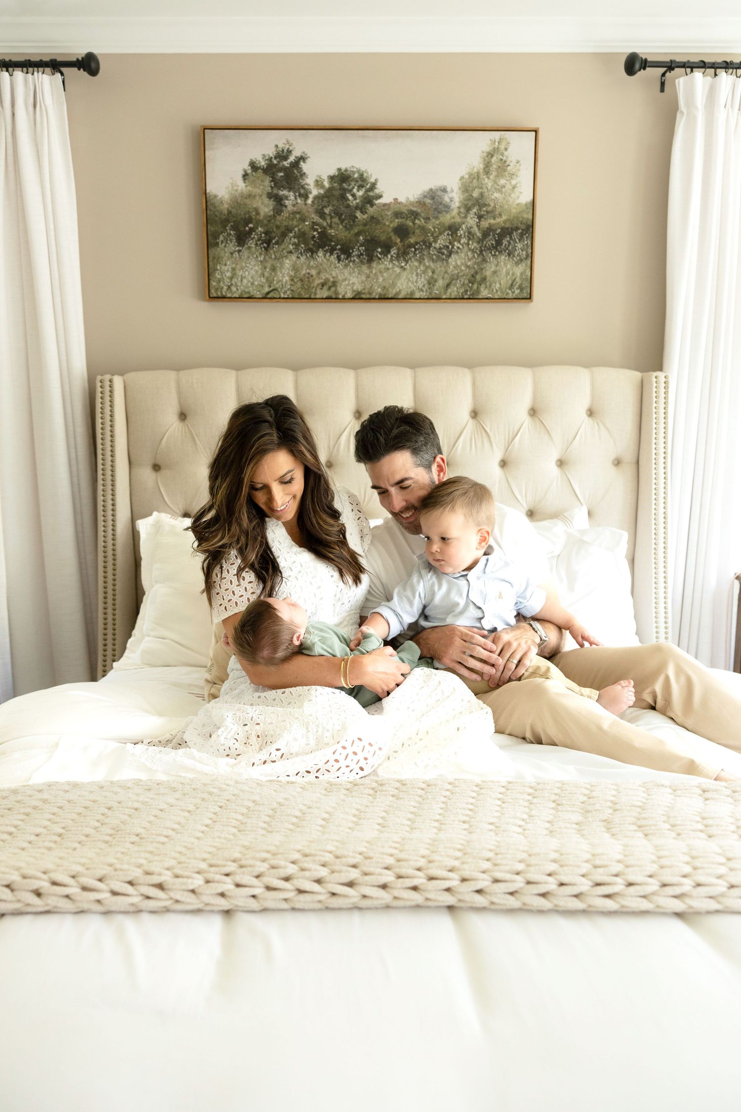 Intimate family photoshoot on a white tufted bed with neutral decor.