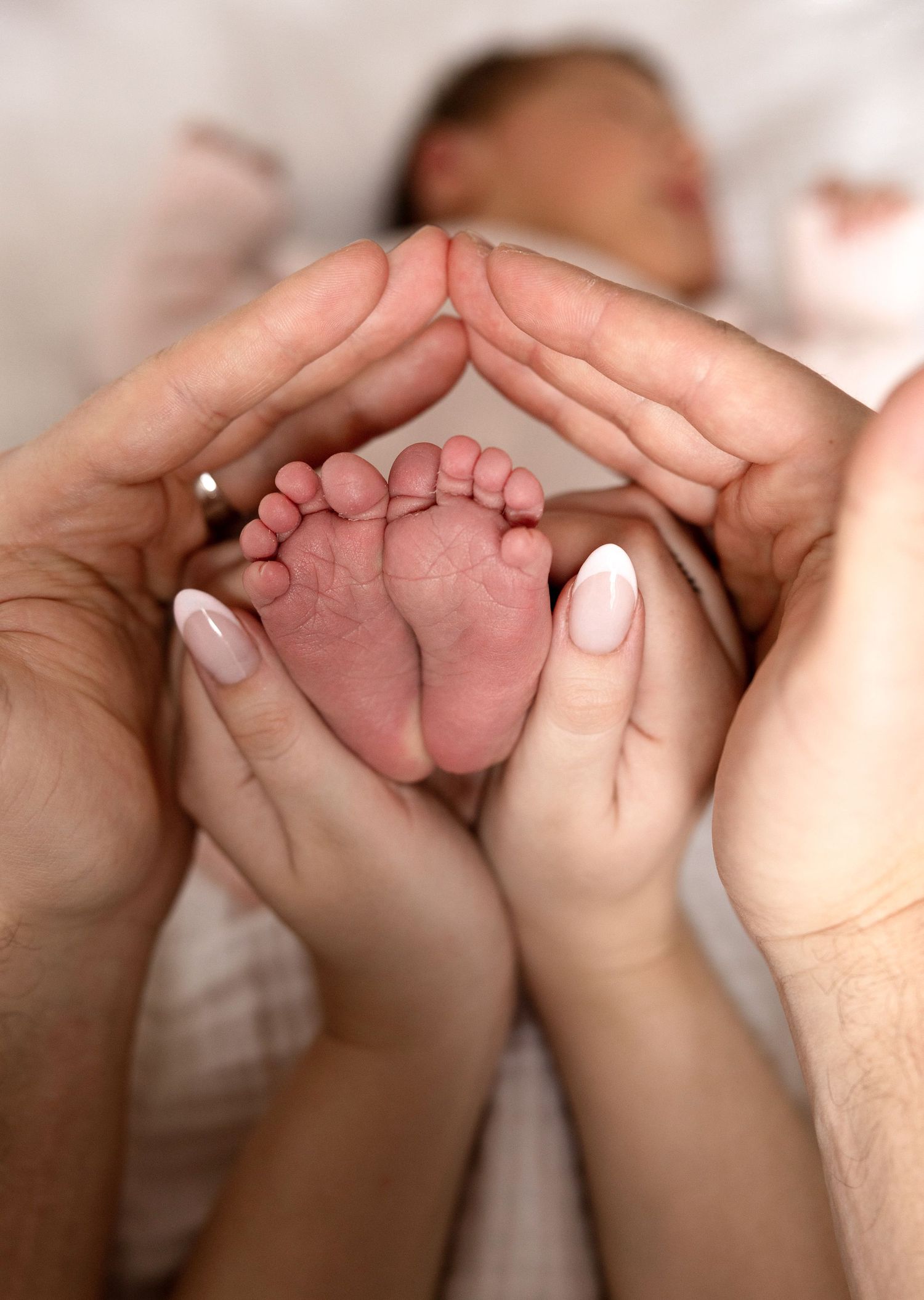 Parents cradle their newborn baby's tiny feet in their hands, forming a heart shape in a tender family moment.