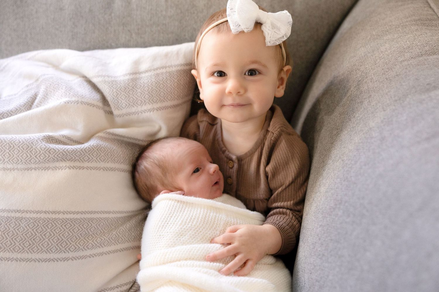 Baby resting peacefully on soft gray couch with white bow accessory.