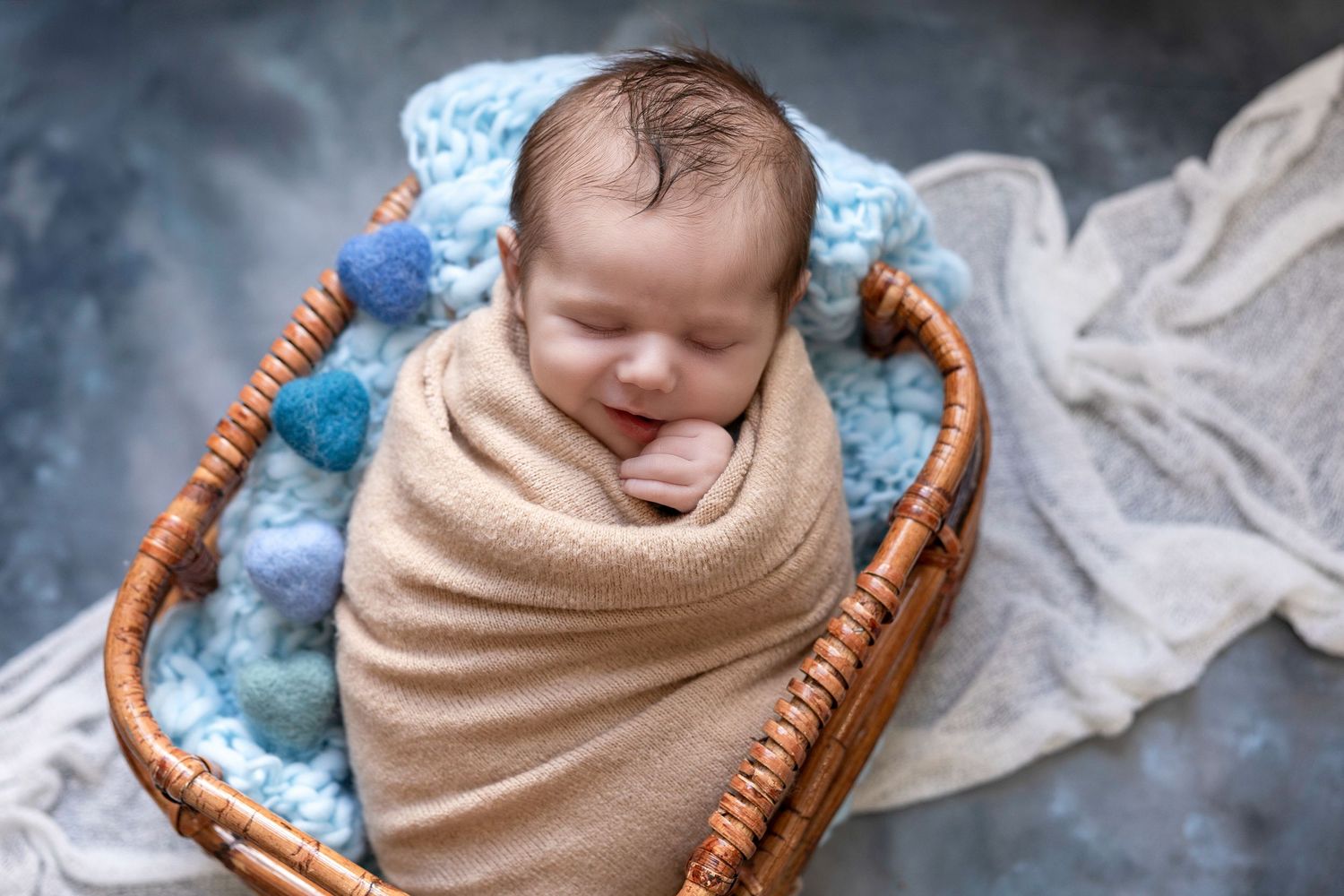 Newborn baby wrapped in beige blanket sleeping peacefully in woven basket.