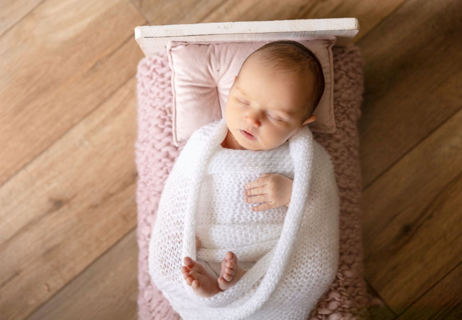 A sleeping infant wearing white rests on a cozy pink blanket.