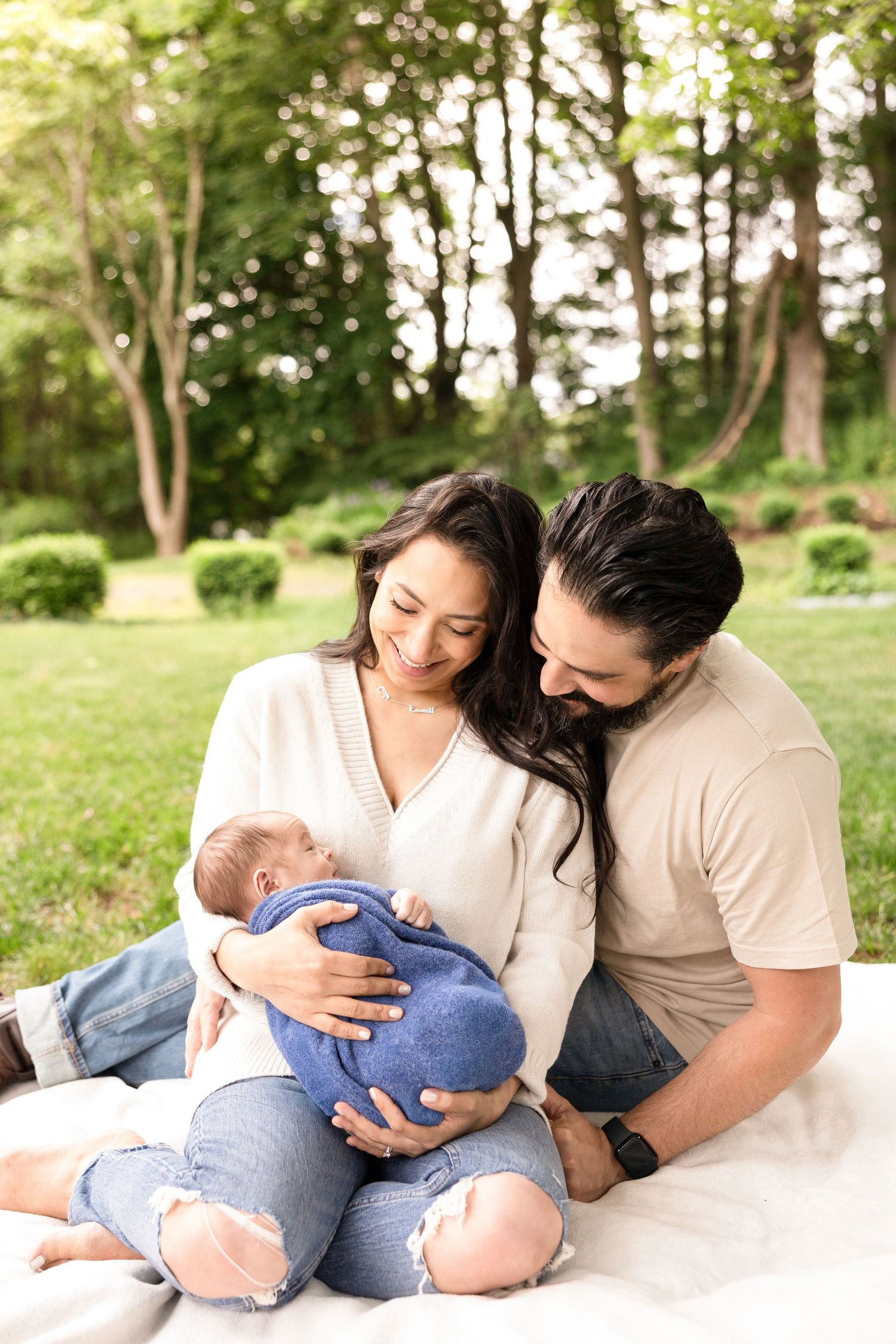 A family shares tender moments on a white blanket outdoors with their baby wearing blue.