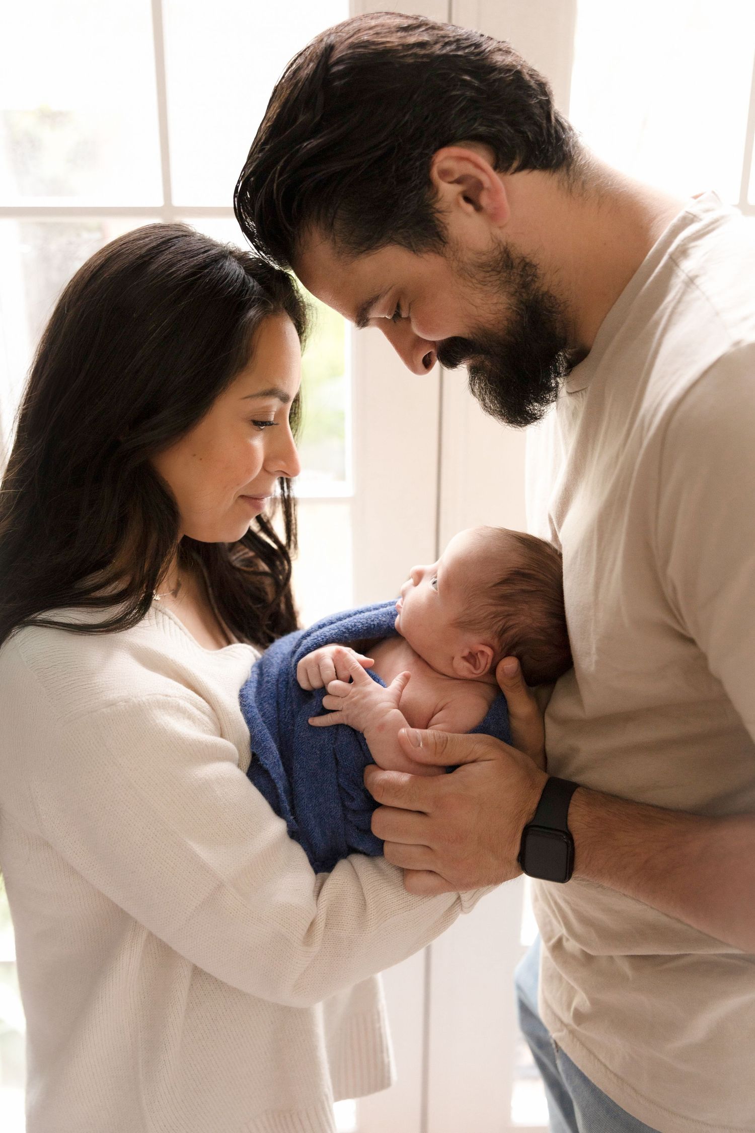 A couple cradles and bonds with their newborn baby in a bright indoor setting.