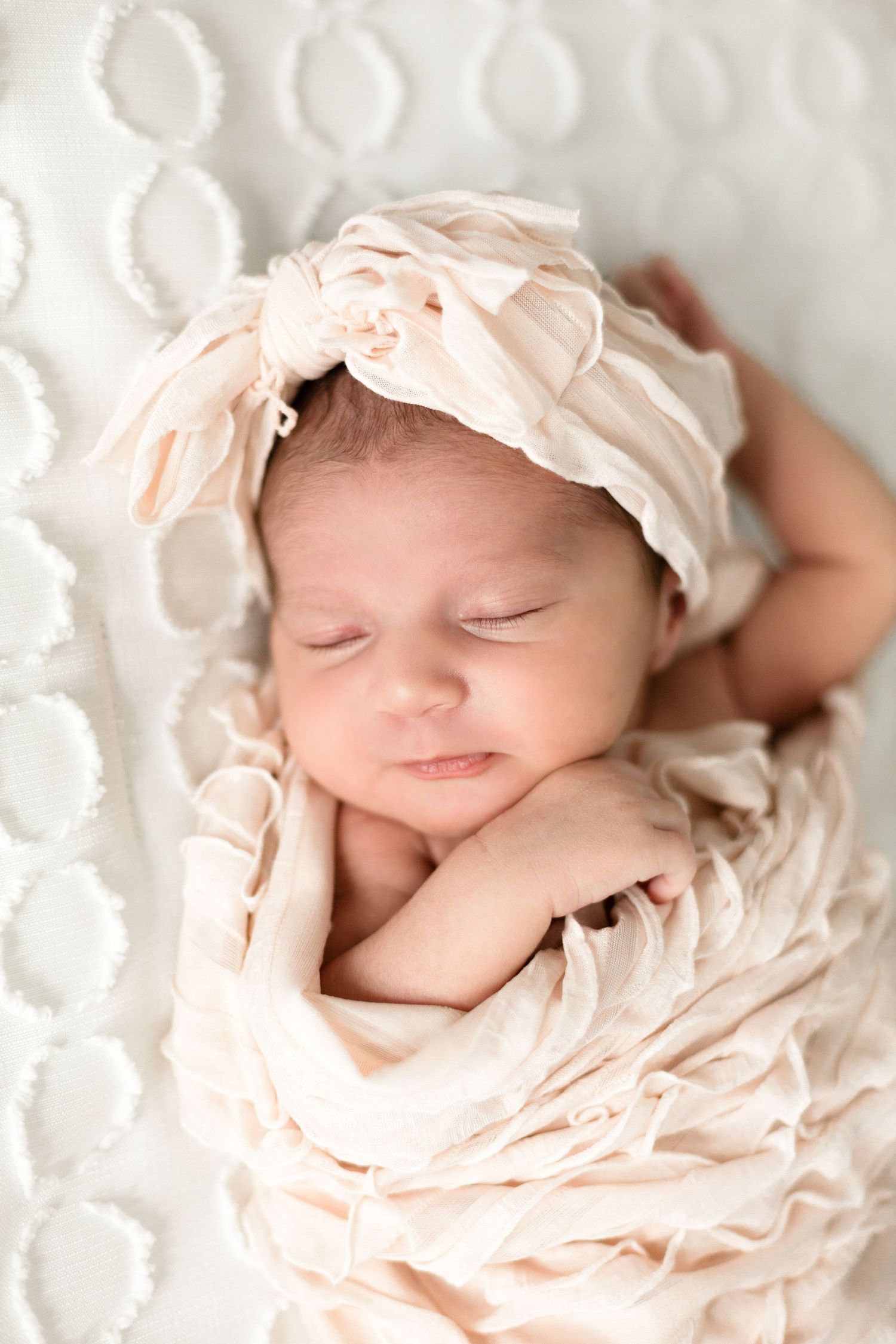 Sleeping newborn baby wrapped in soft peach fabric wearing a matching headband.