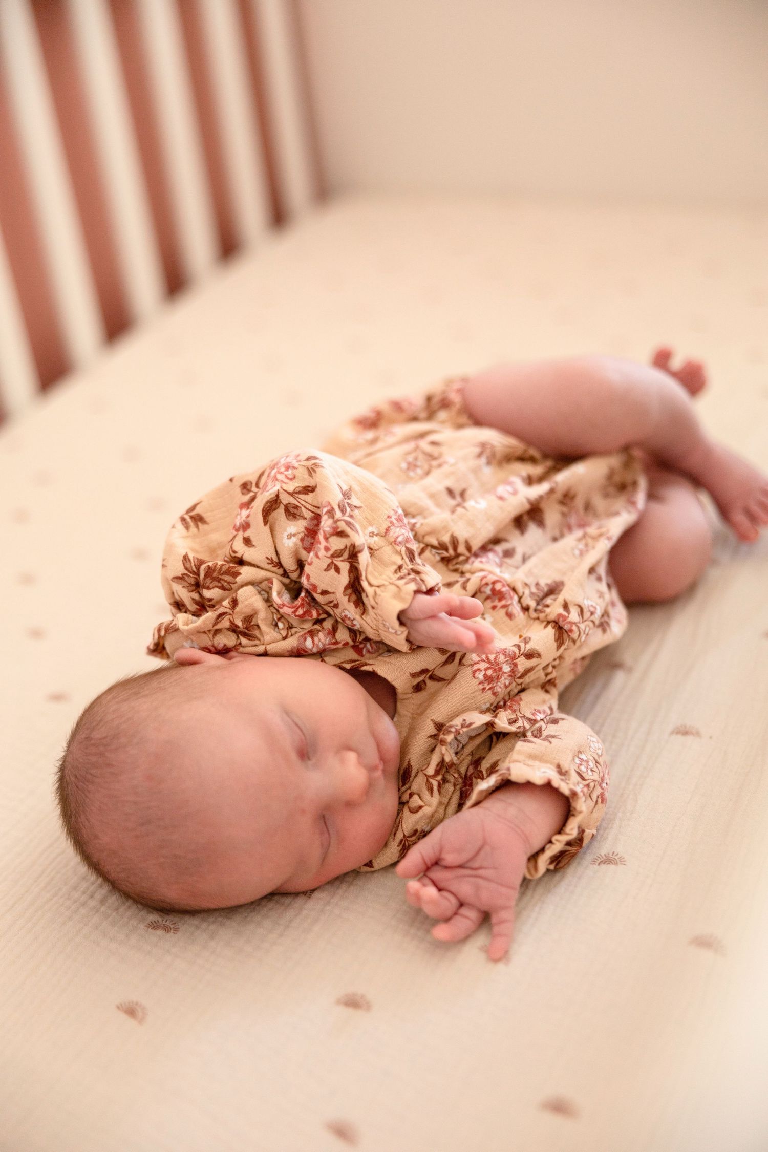 A sleeping newborn in floral outfit lies peacefully on wooden surface.