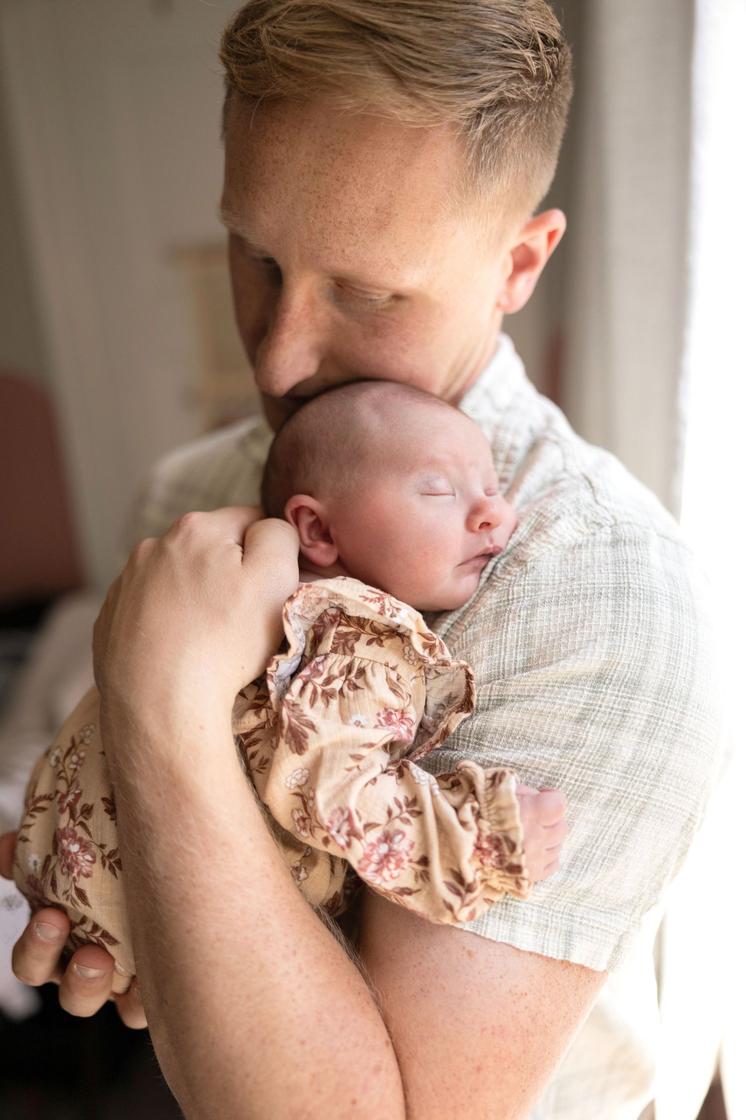 A parent tenderly holds and kisses their newborn wearing floral clothing.