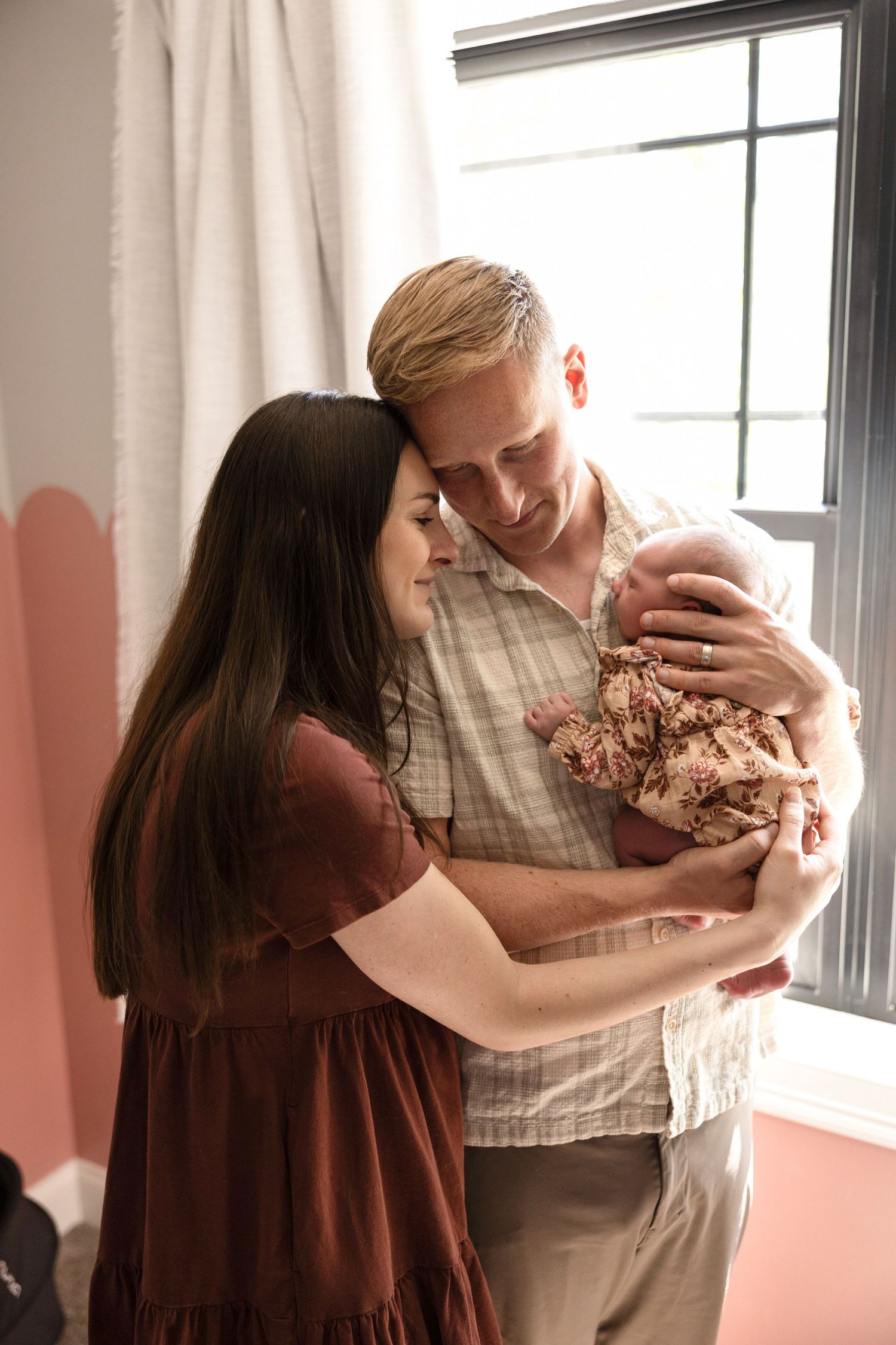 Parents share loving moments with their newborn by a sunlit window.