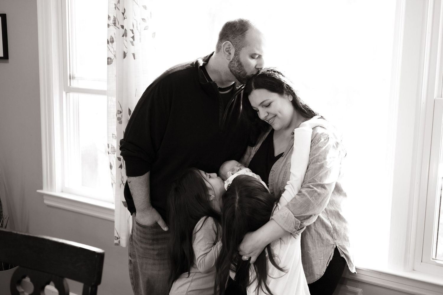 Natural light family portrait session by large window showing tender moments.