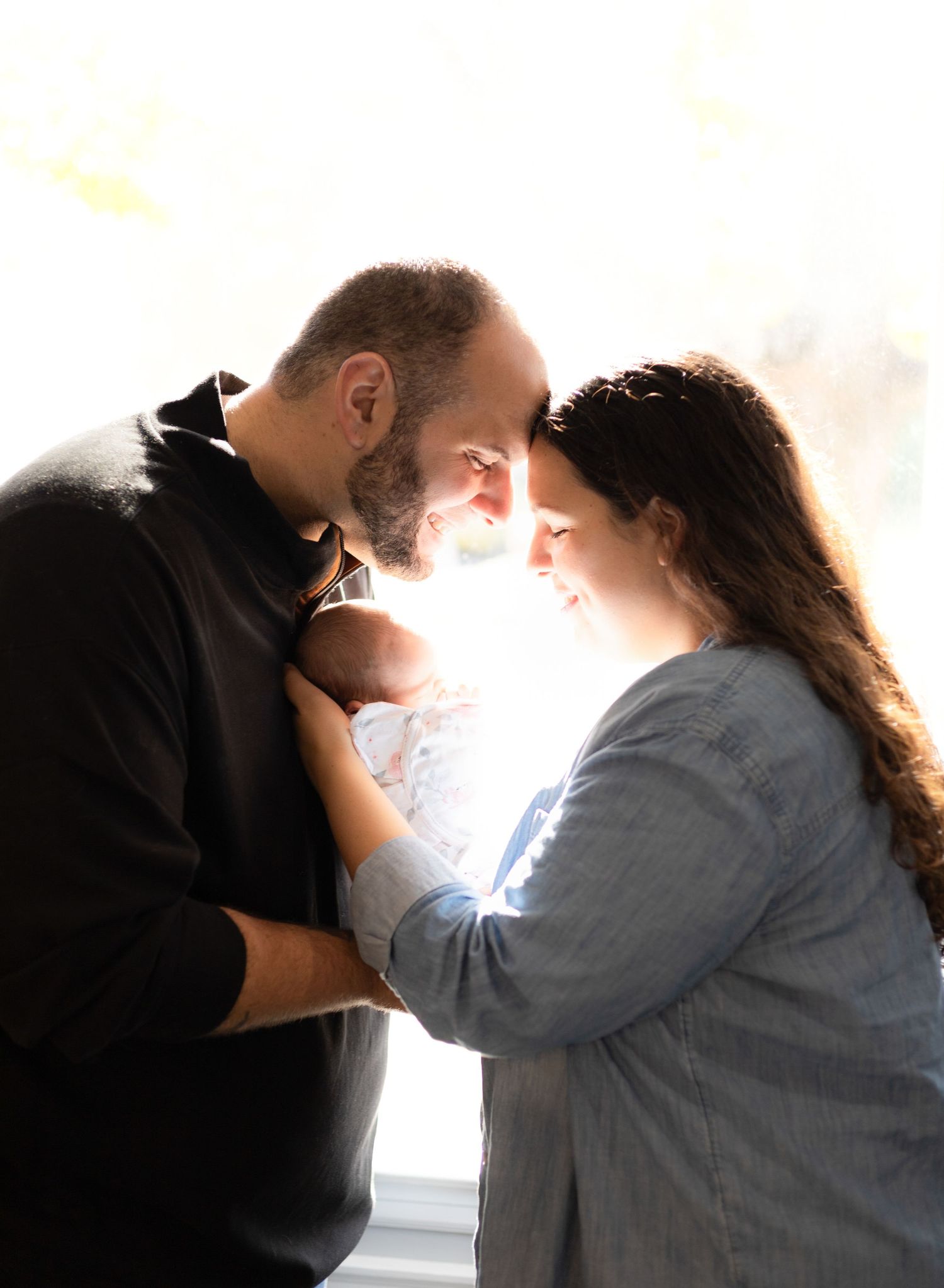 Backlit family photography session creating silhouettes against bright window.