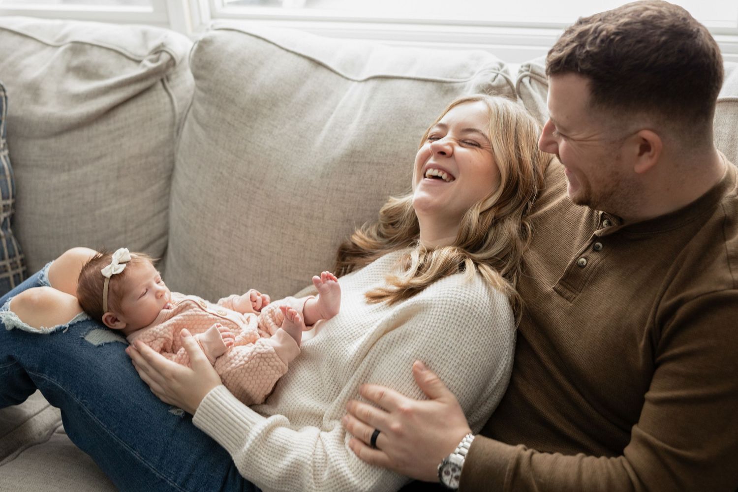 Family relaxes together on beige couch during casual home photography session.