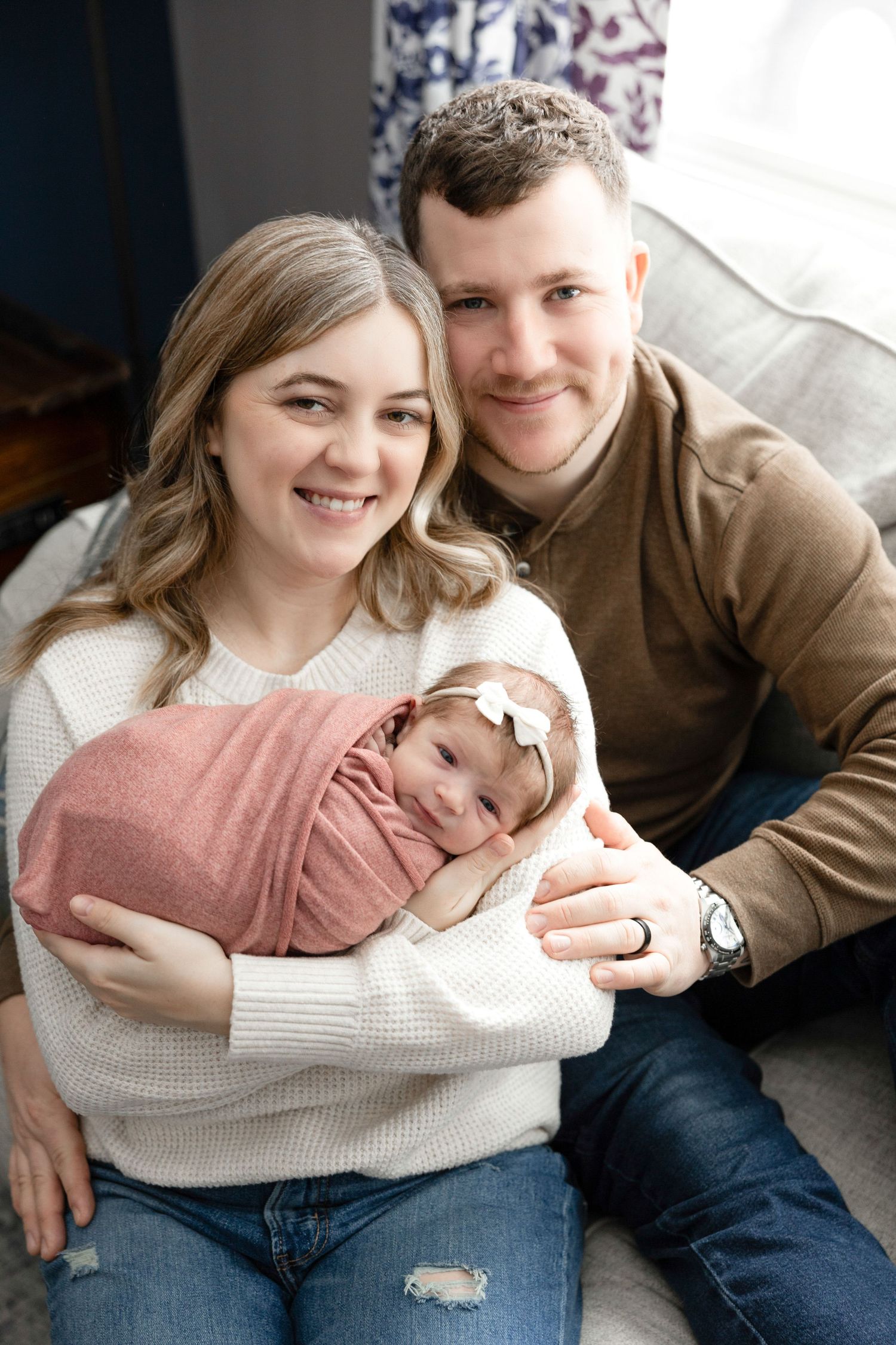 Lifestyle family portrait with parents cuddling on couch in casual setting.