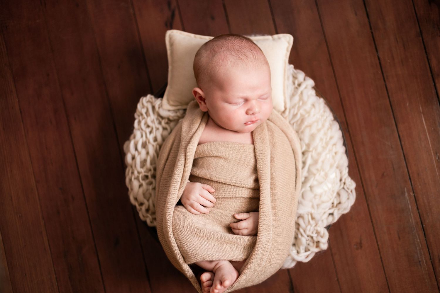 Newborn baby photography series on wooden floor with cream colored blanket.