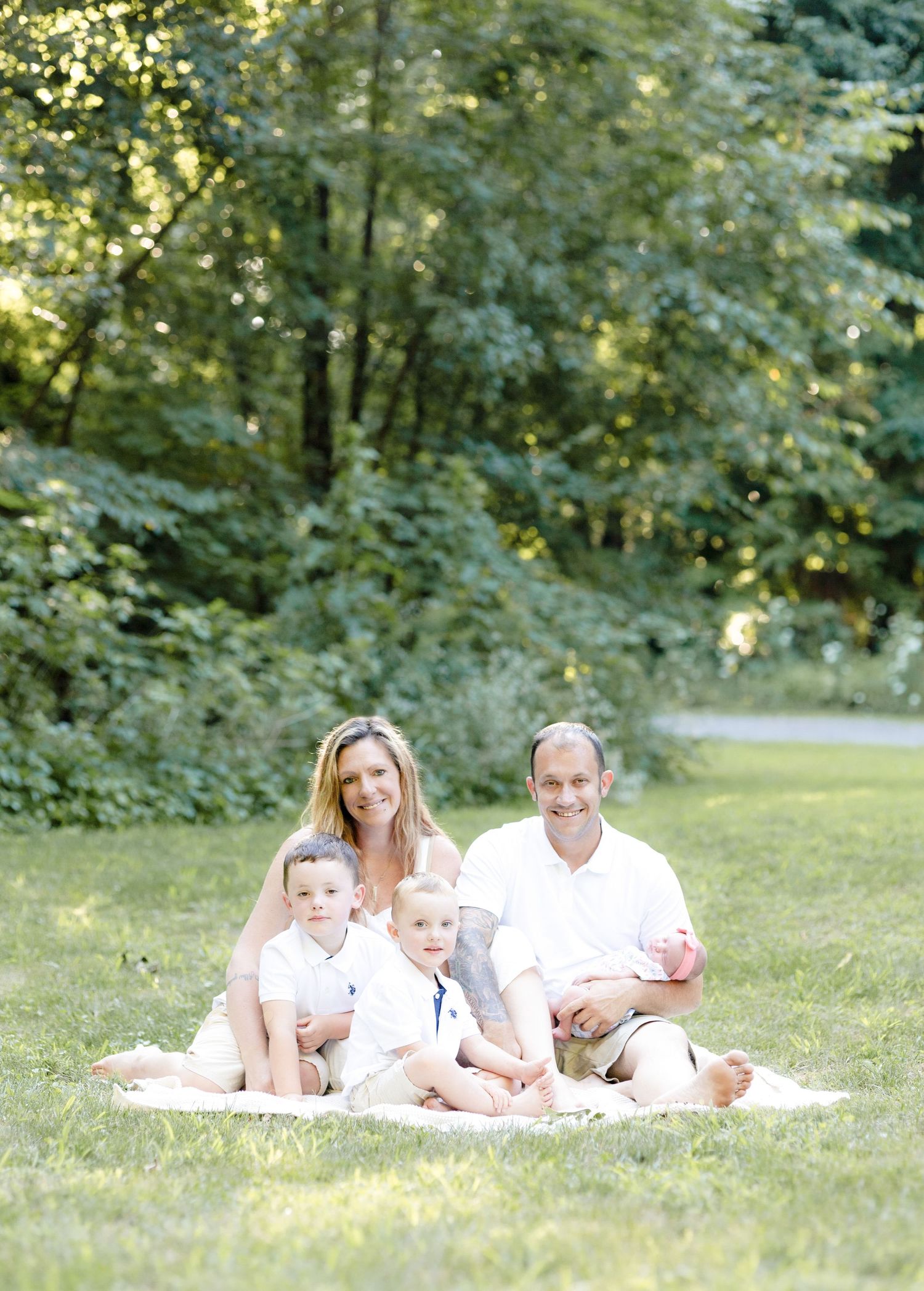 Family relaxing together on grassy lawn with trees in summer setting.