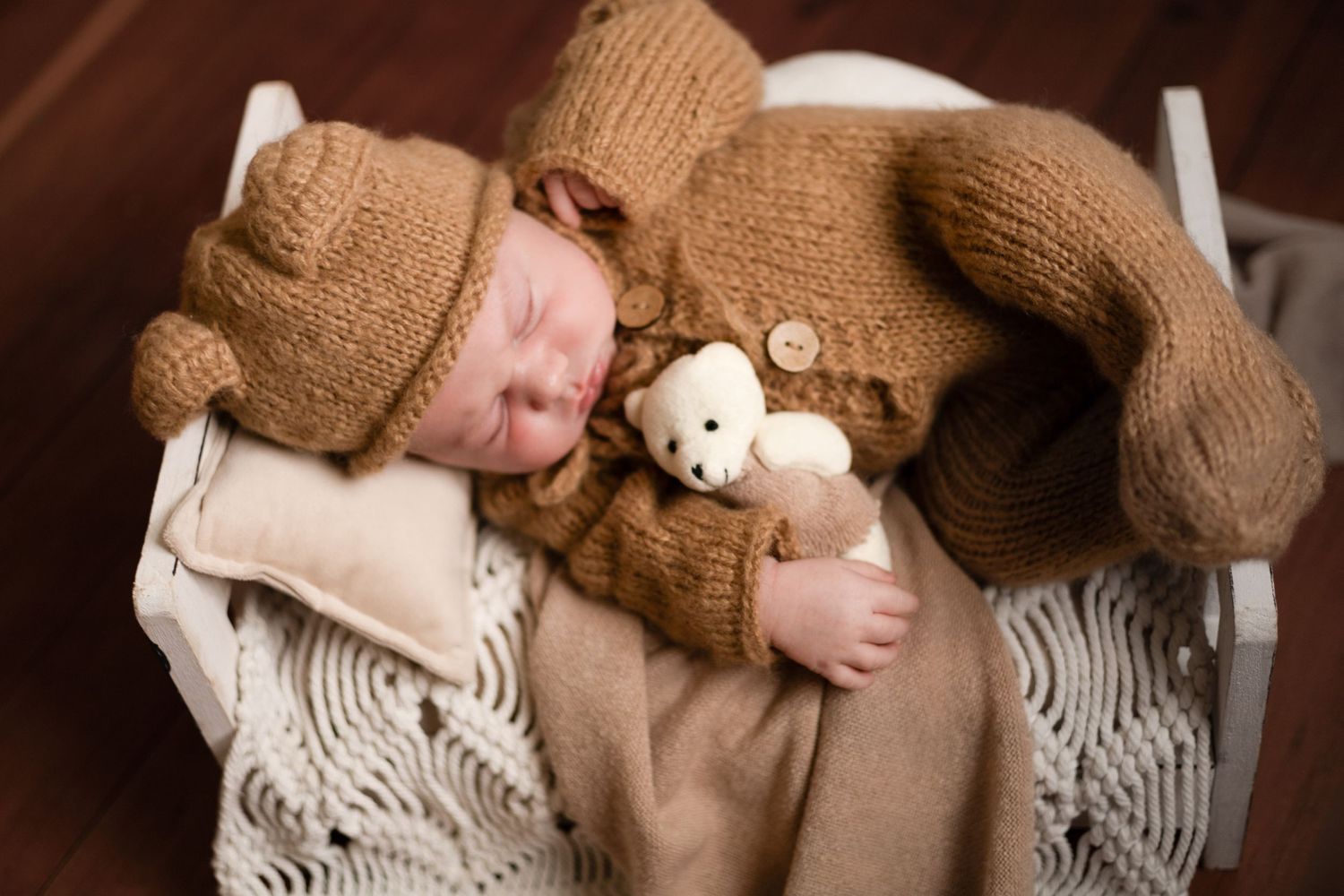 Baby in cozy knit outfit with teddy bear on white textured blanket.