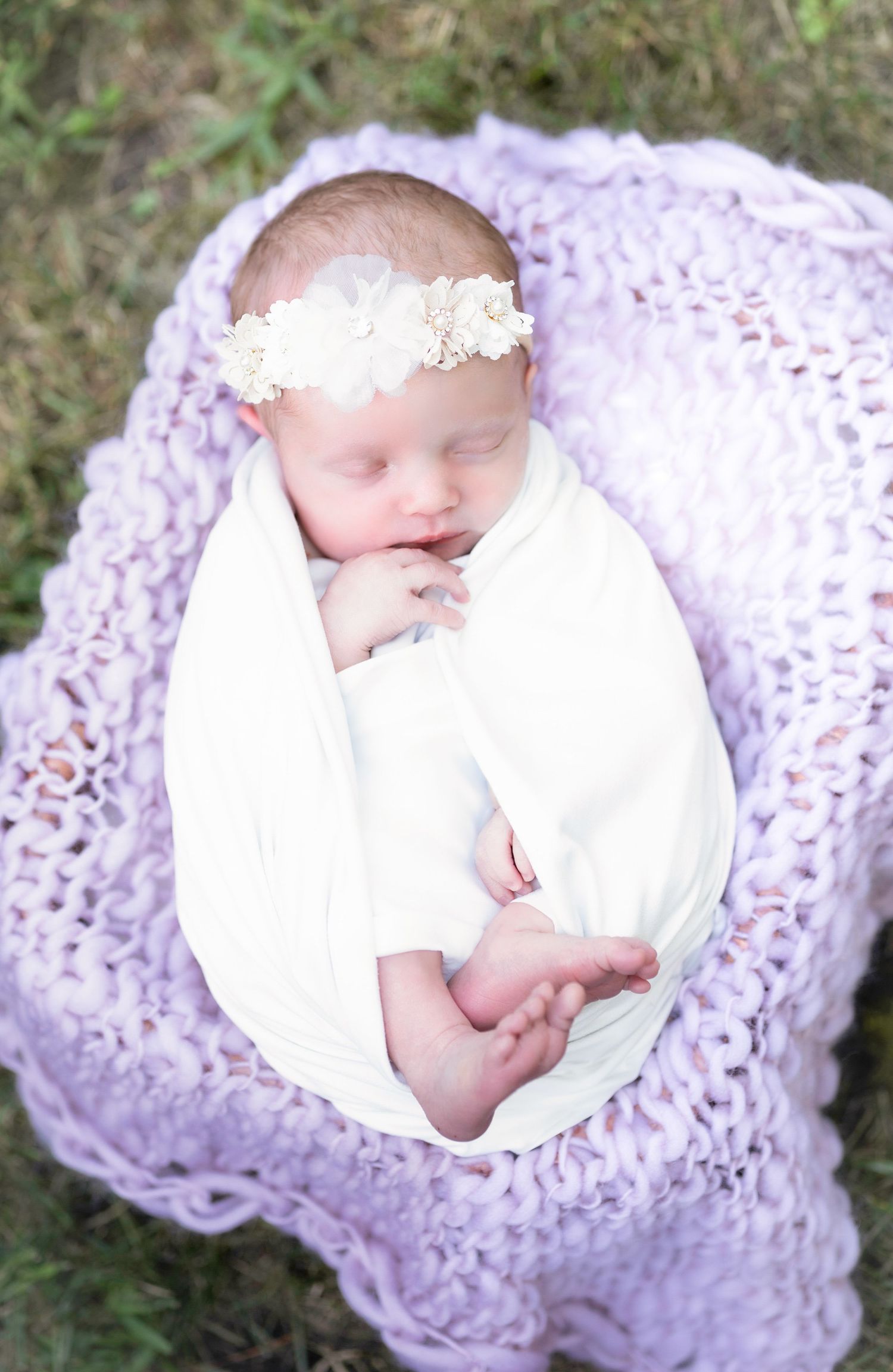 Newborn baby sleeping peacefully on purple knitted blanket outdoors.