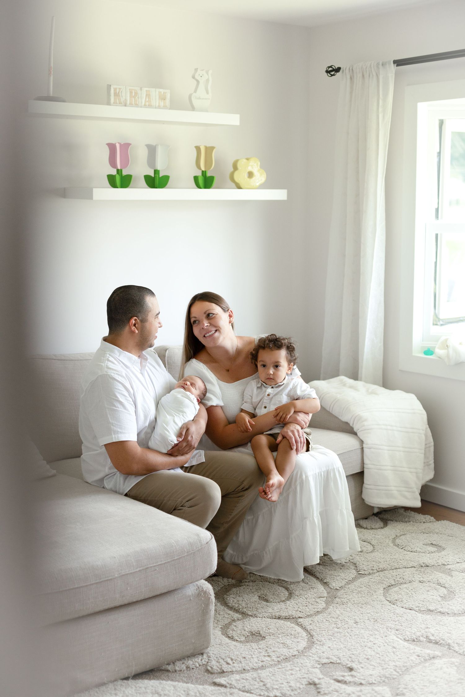 Family relaxing together on a white couch in a bright nursery decorated with colorful tulip ornaments.