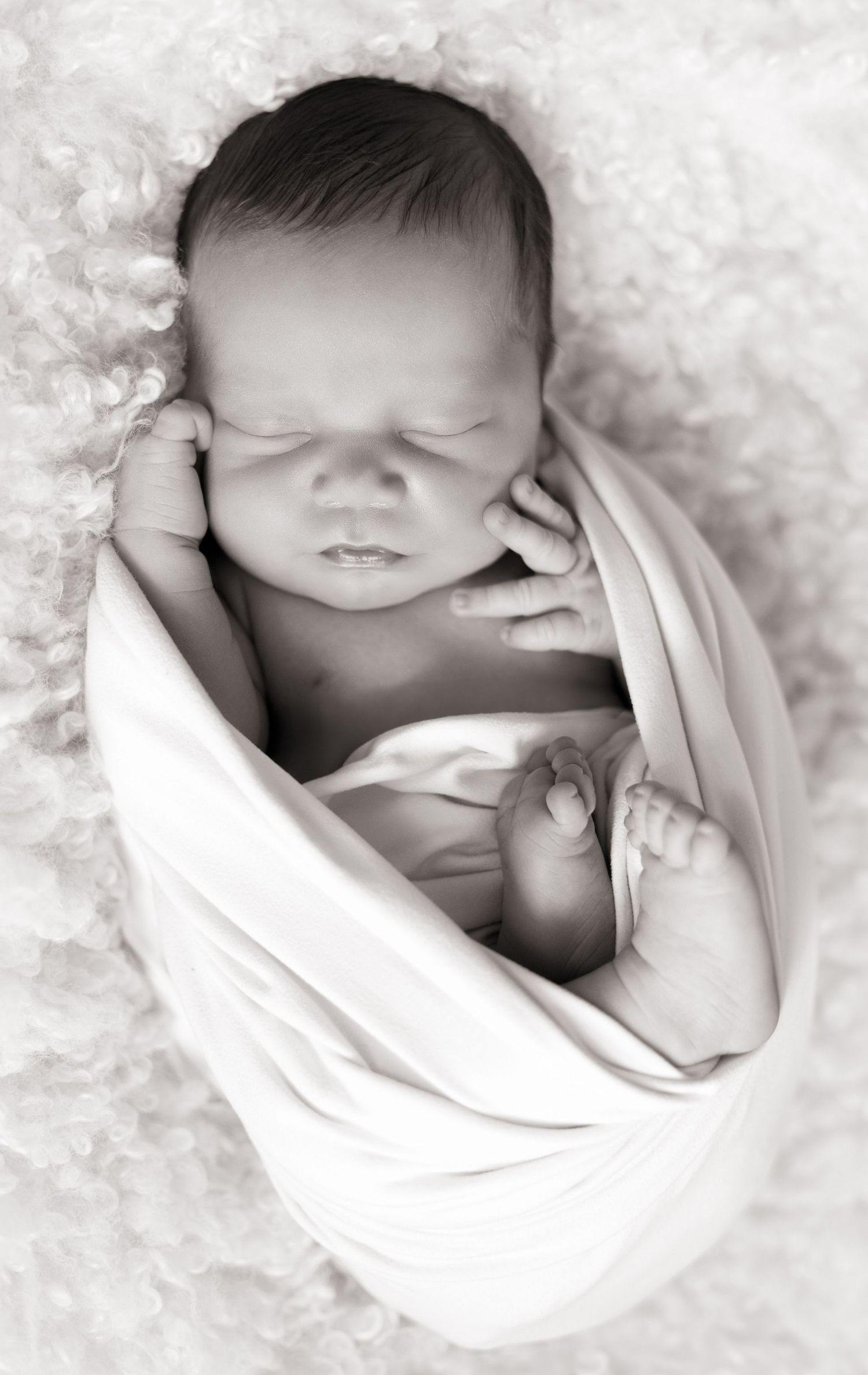 Peaceful sleeping newborn wrapped in white fabric against soft textured background.