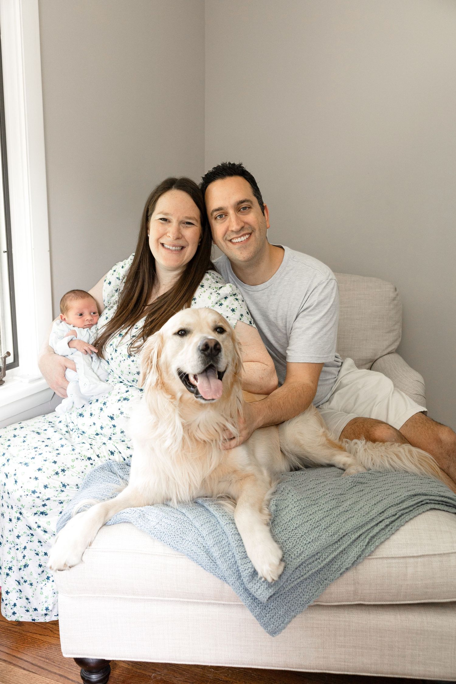 Family photos on white couch with golden retriever dog and baby in casual setting.