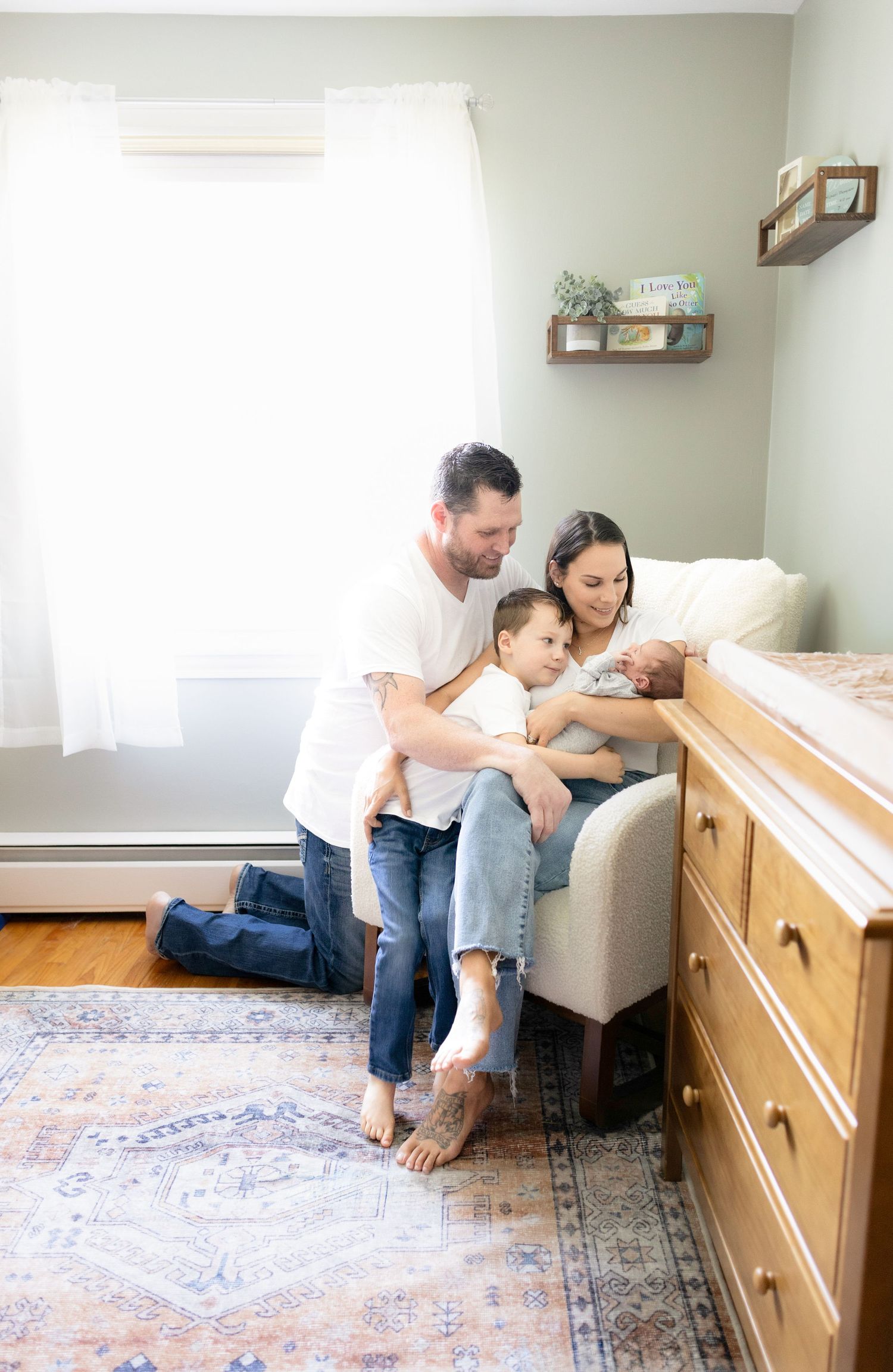Family sitting together on floor near wooden furniture in bright room.