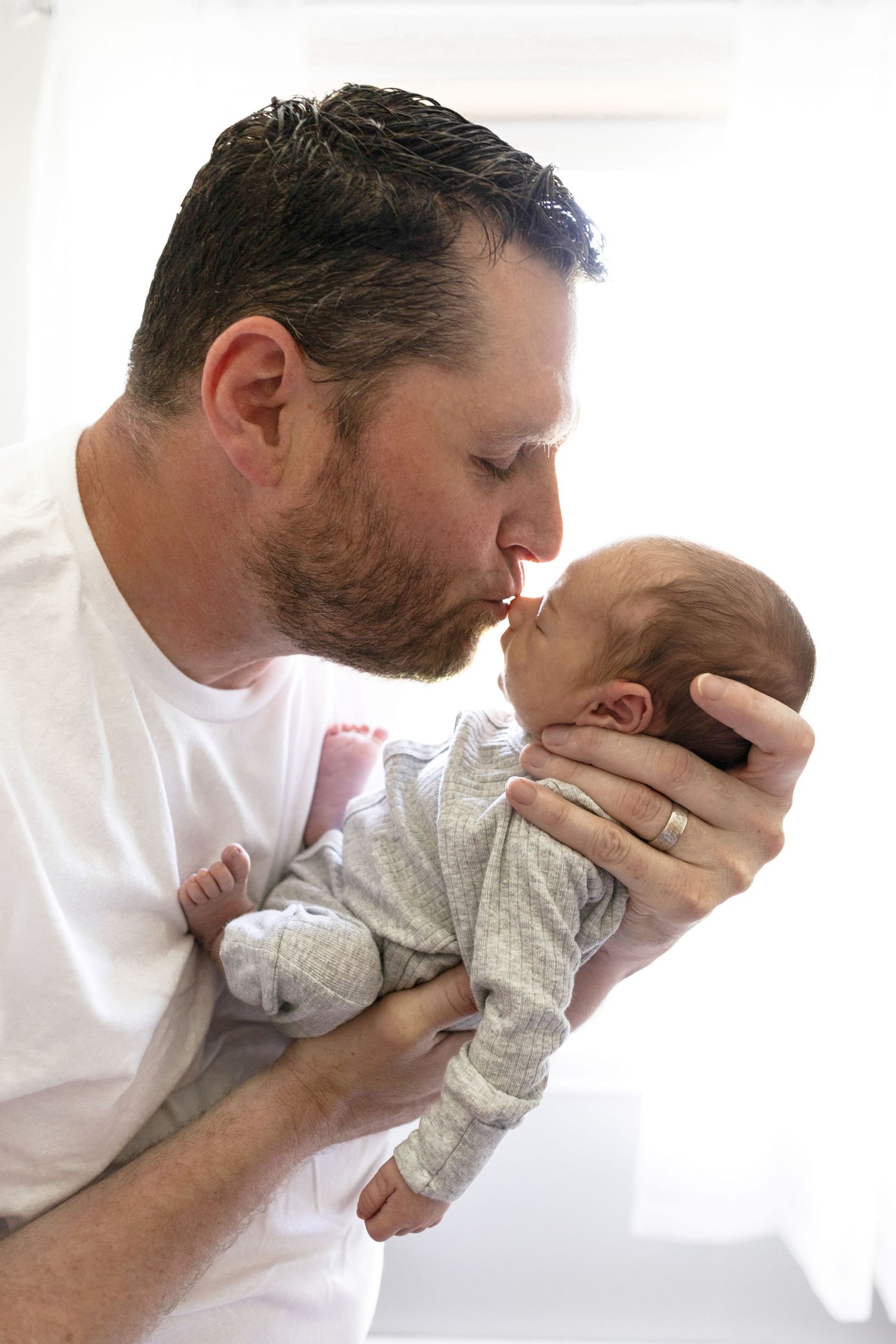 Parent giving affectionate kisses to baby in white room.