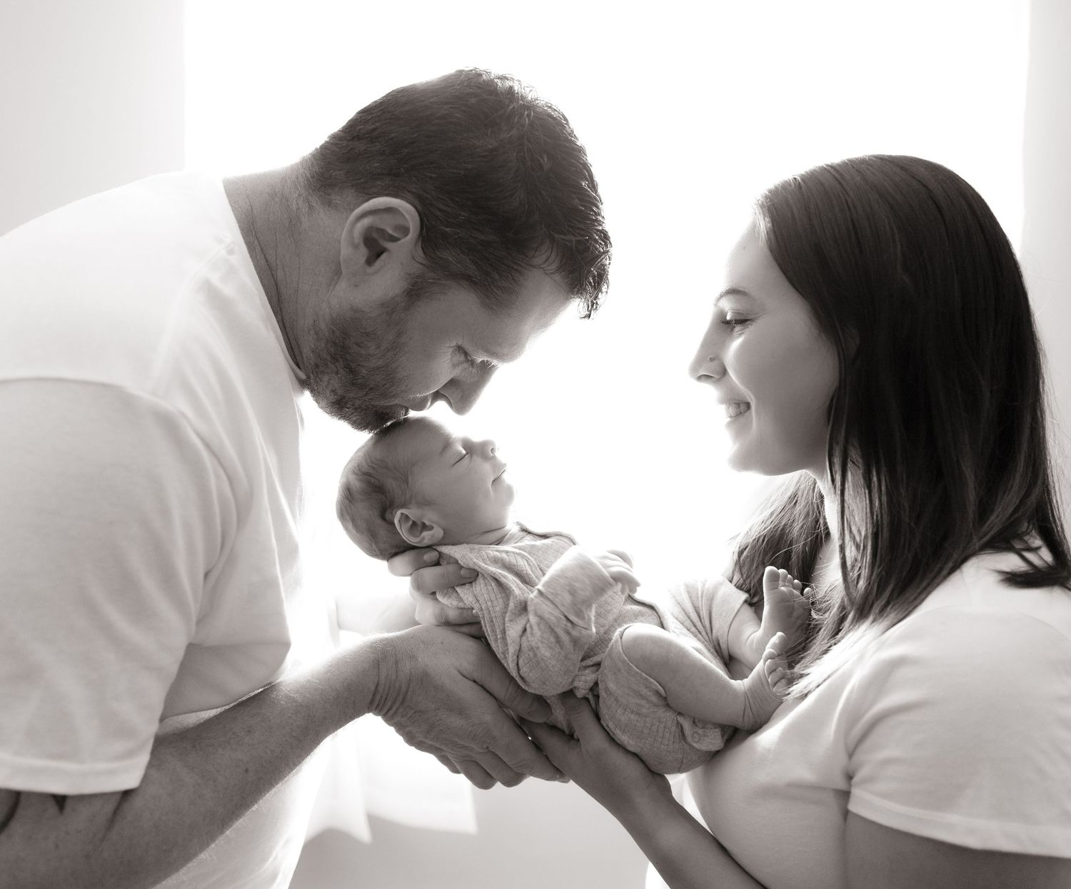 Black and white portrait of parent kissing baby.