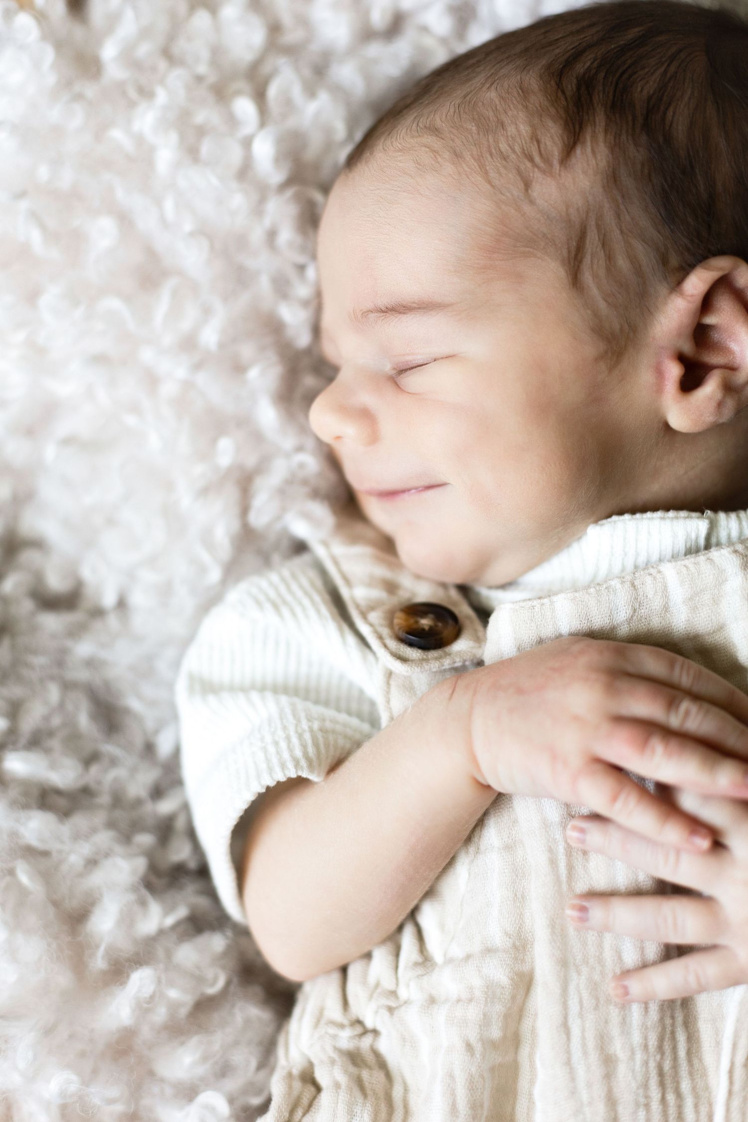 Sleeping baby in white knit outfit on textured background.