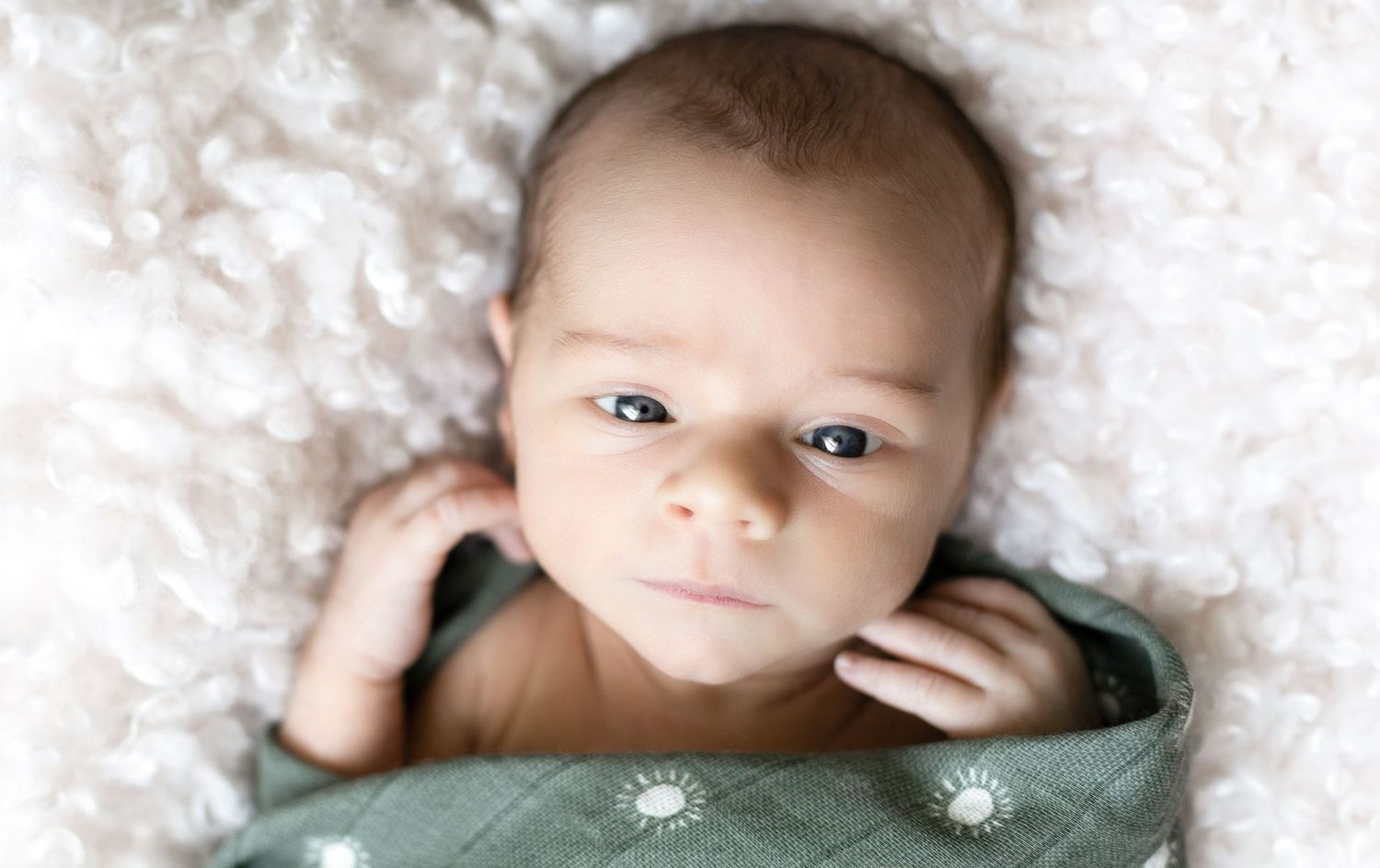 Baby lying on white textured blanket looking at camera.