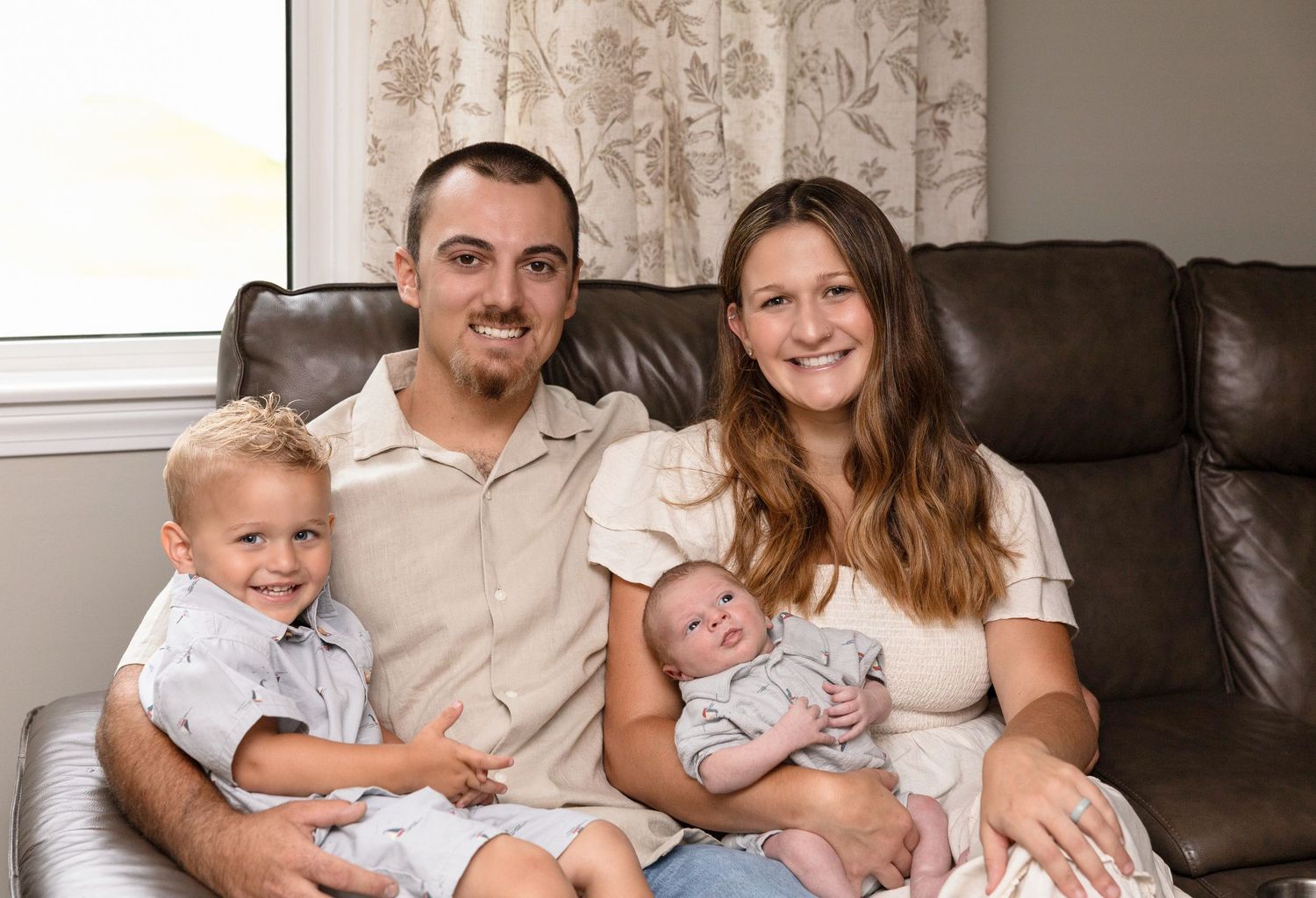 Family portrait session on brown leather couch in natural light setting.