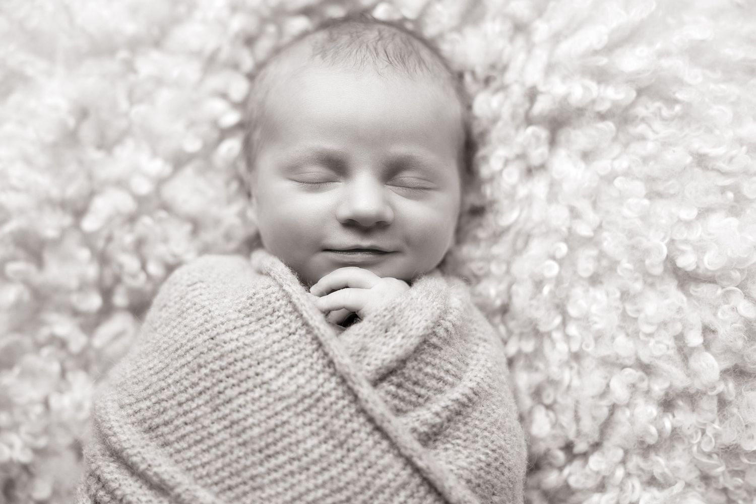 Black and white photos of a sleeping newborn wrapped in soft textured blankets.