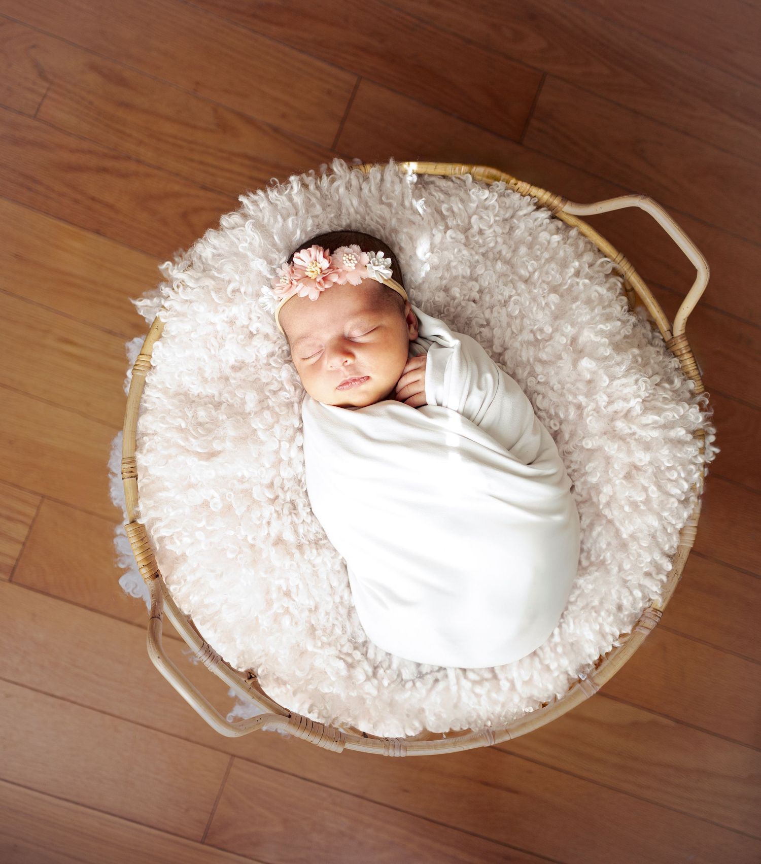 Newborn baby wrapped in white swaddle on circular white rug.