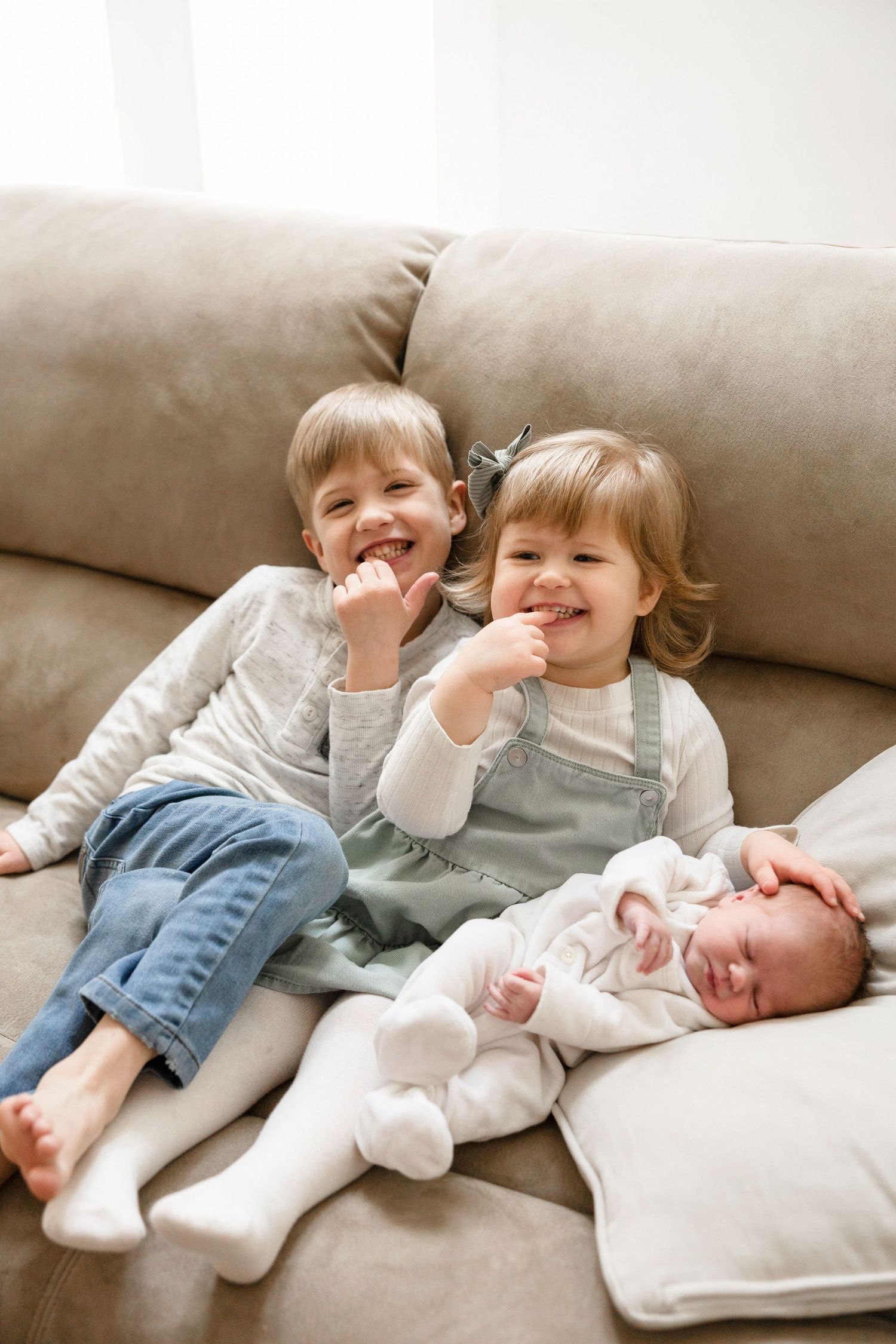 Children share joyful moments on a couch while meeting their new baby sibling.