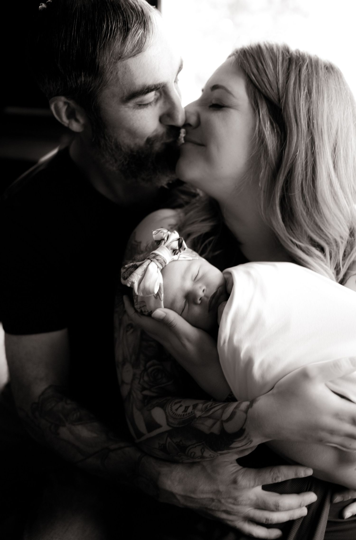 Black and white intimate portrait of couple sharing tender moments with their newborn.