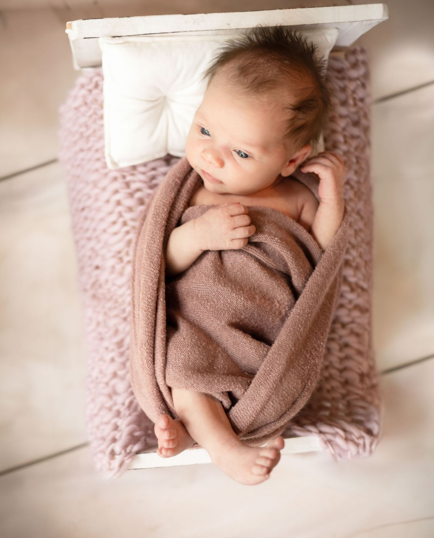 Newborn baby sleeping peacefully on pink textured blanket in soft natural light.