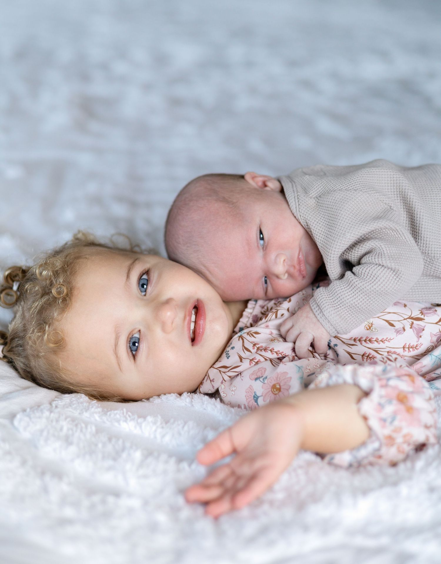 Child lying on white textured blanket in delicate floral outfit.