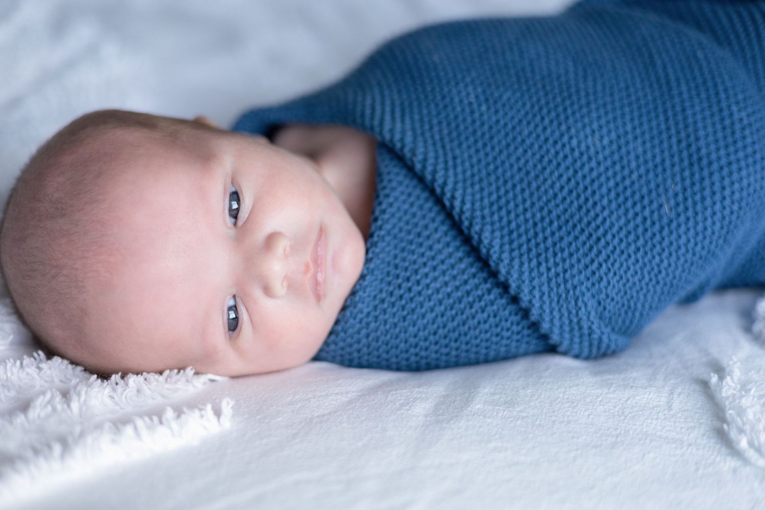 Baby in blue sweater resting on white textured surface.
