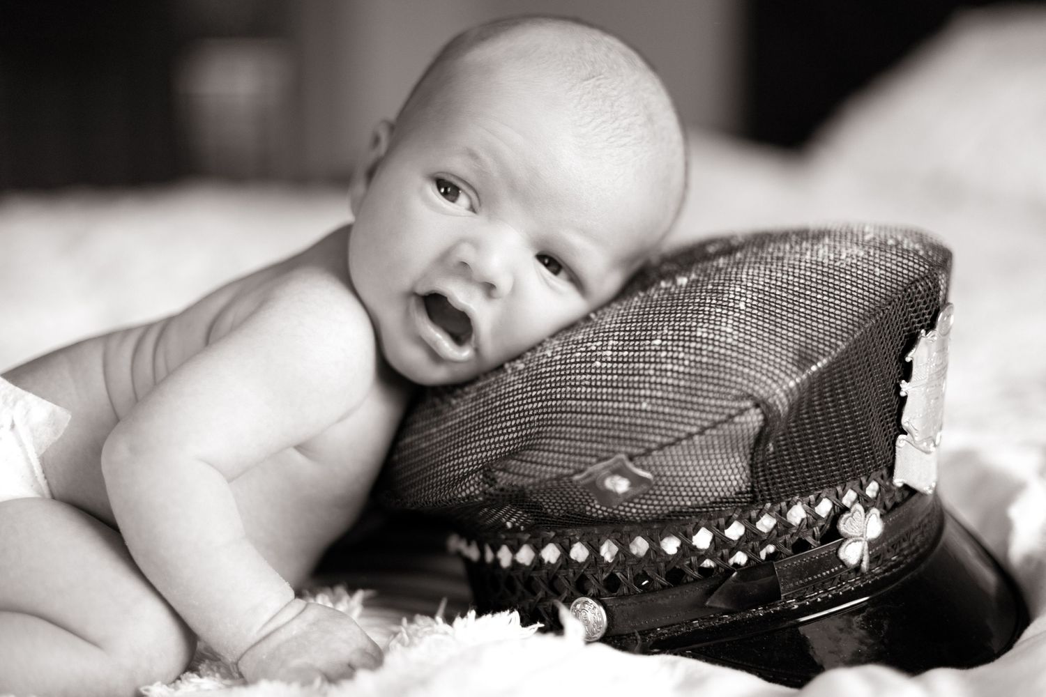 Baby resting on dark cushion with decorative beaded trim in black and white photo.