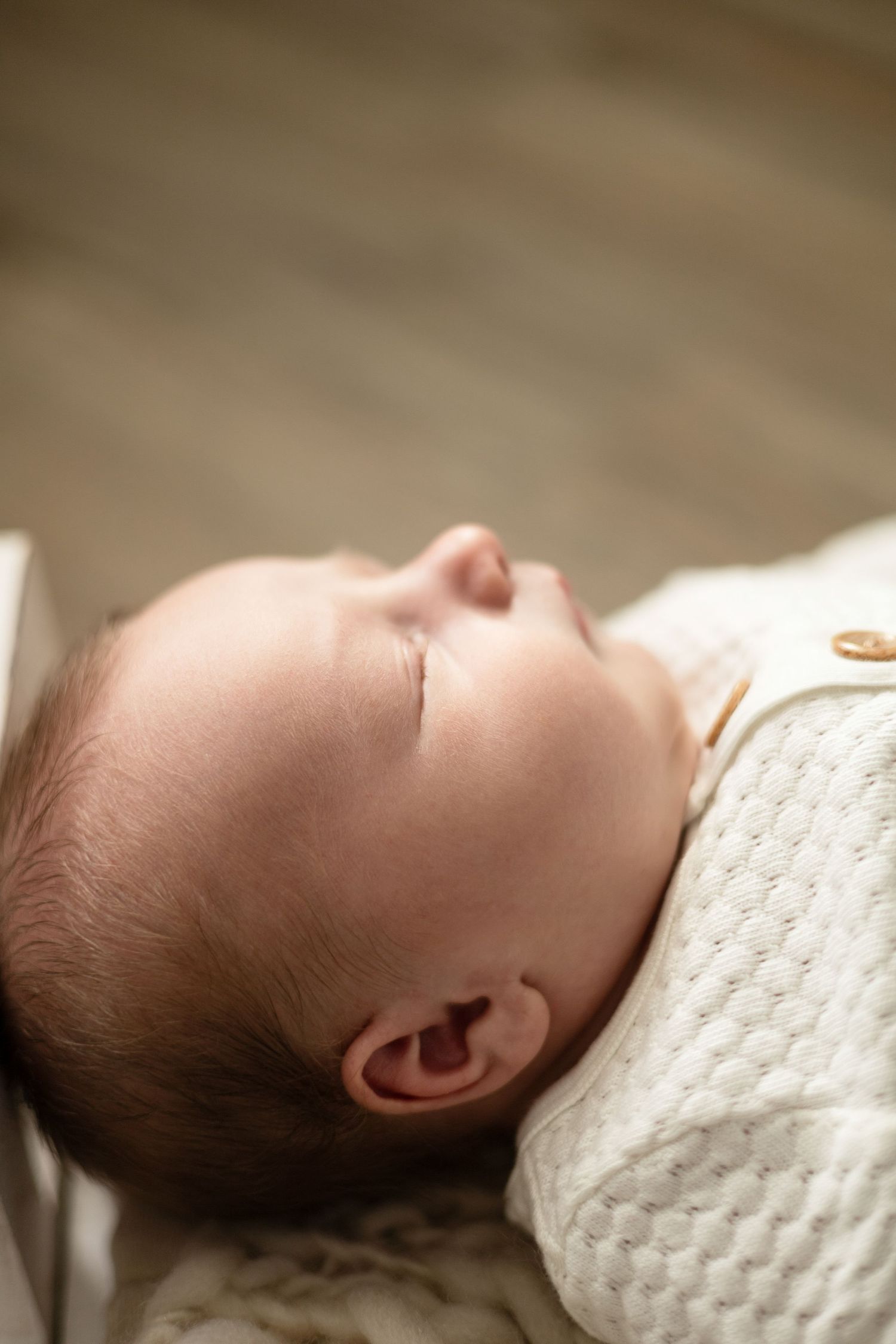 Peaceful sleeping newborn wearing white knit clothing in soft lighting.