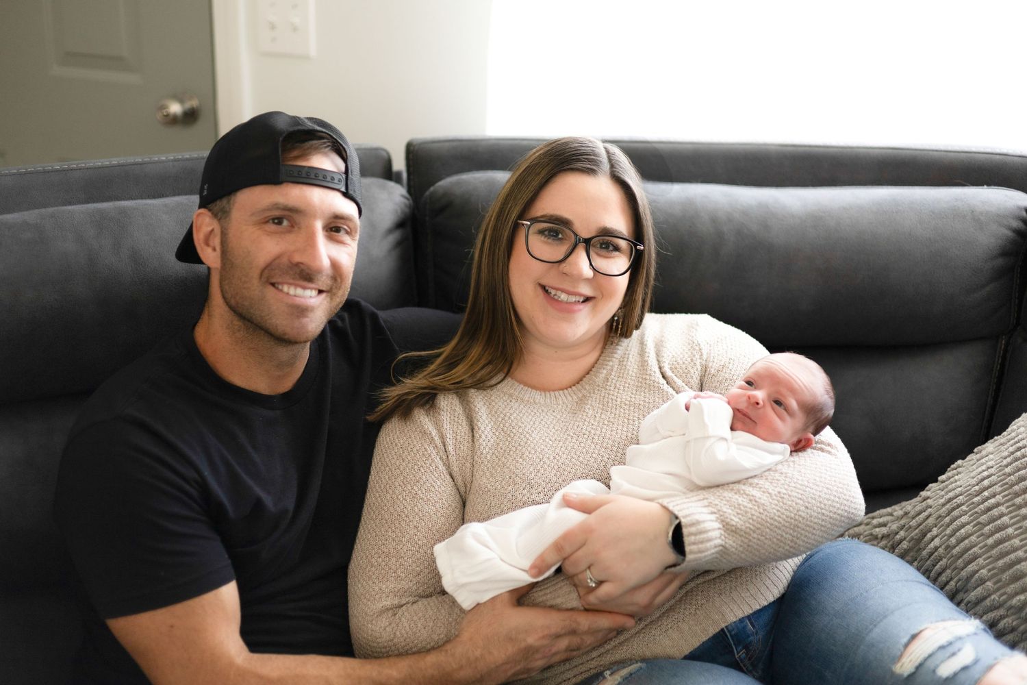 Candid family moment on dark leather couch with newborn in cozy home environment.