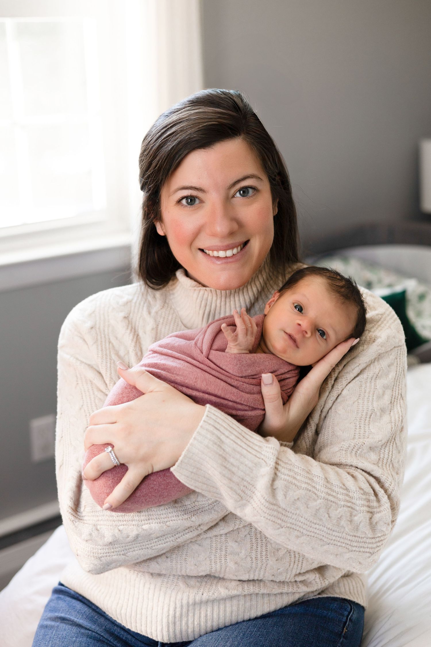 Mother and baby share tender moments in cozy white sweaters while relaxing on bed.