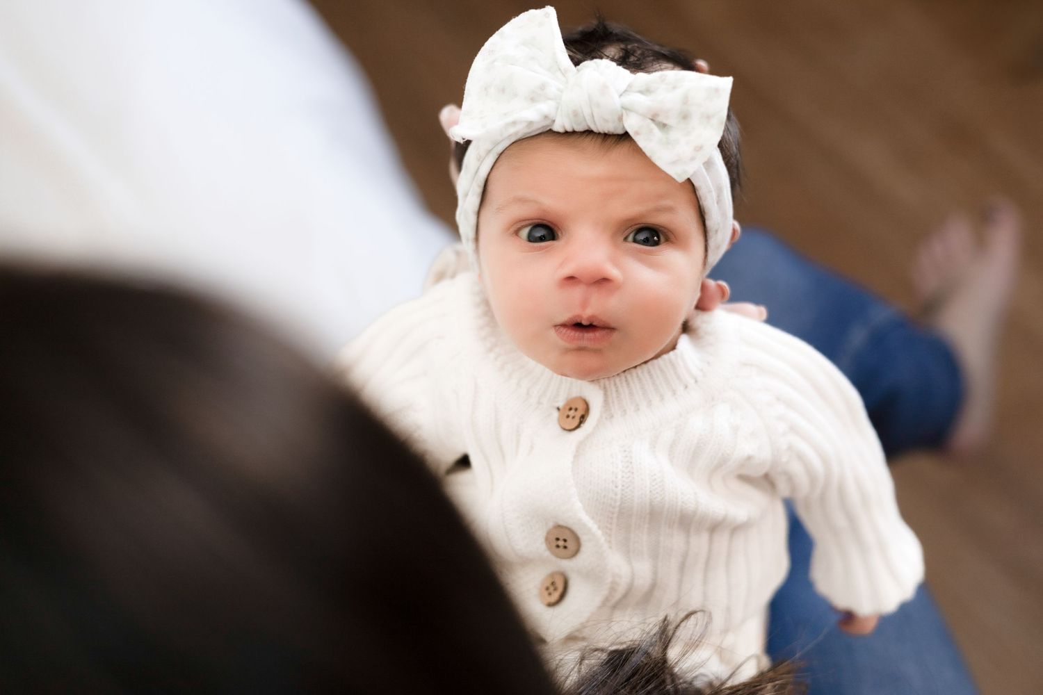 Close-up portrait of baby wearing white knit sweater with decorative buttons.
