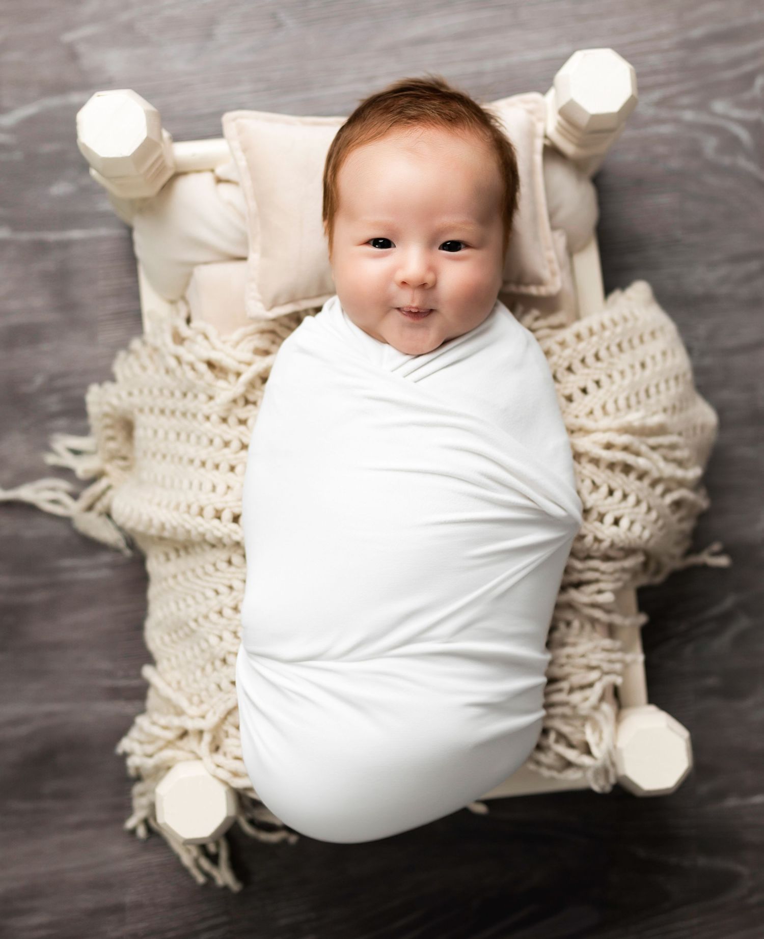 Baby wrapped in white swaddle on cream knit blanket.