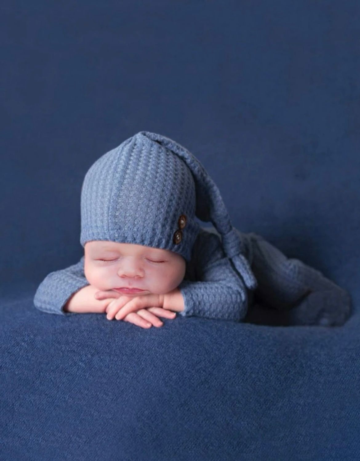 Artistic newborn photography on dark blue background with matching knit hat.